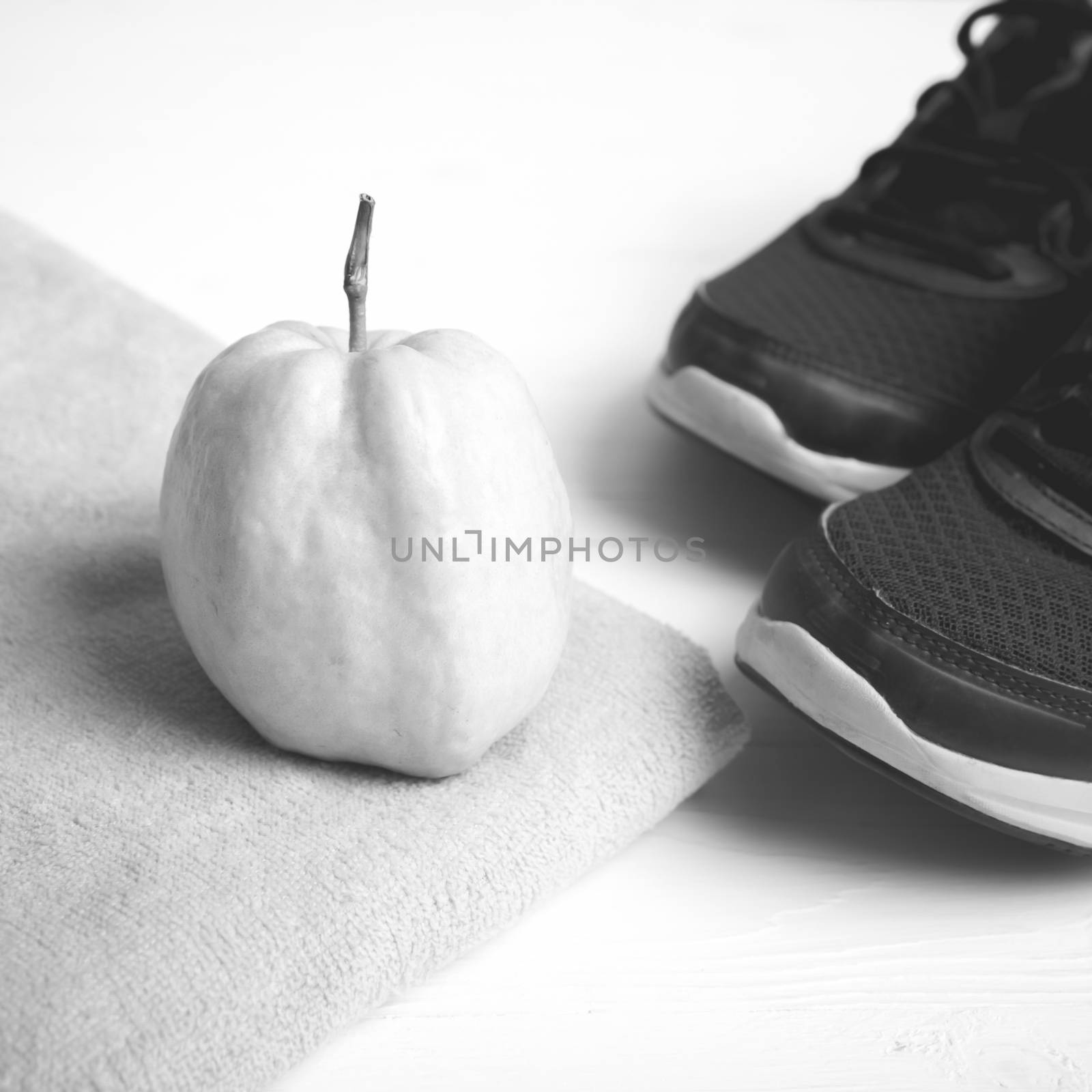fitness equipment : running shoes,towel and guava fruit on white wood table black and white color style