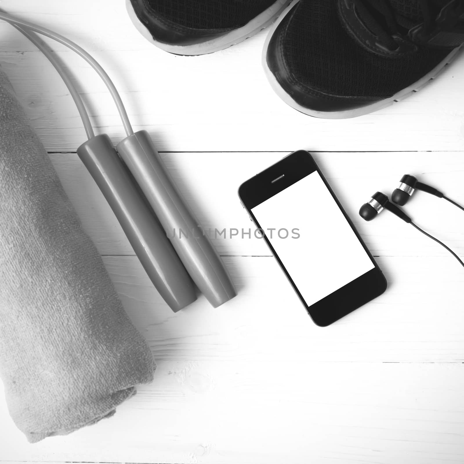 fitness equipment : running shoes,towel,jumping rope and phone on white wood table black and white color tone style