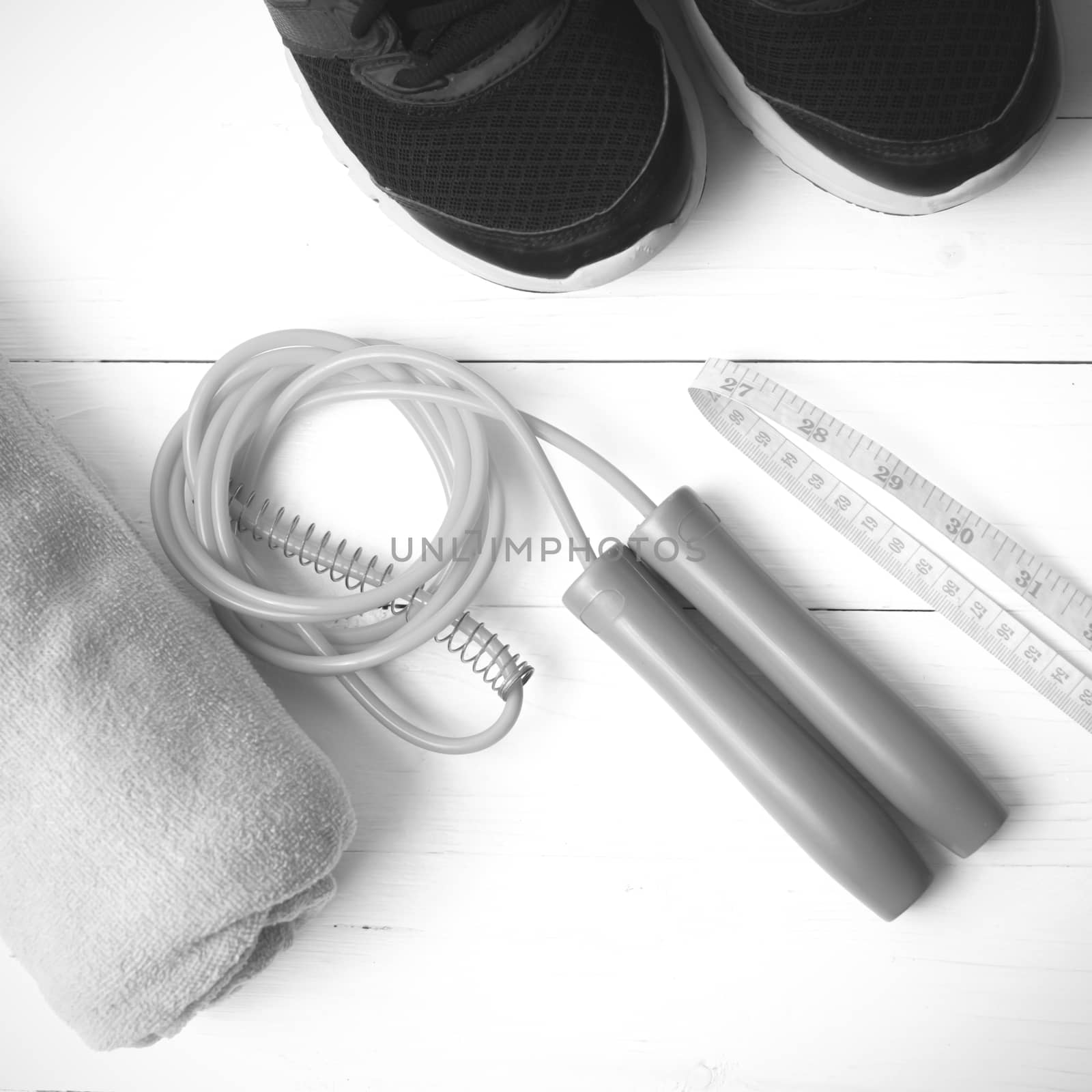 fitness equipment : running shoes,towel,jumping rope and measuring tape on white wood table black and white color tone style
