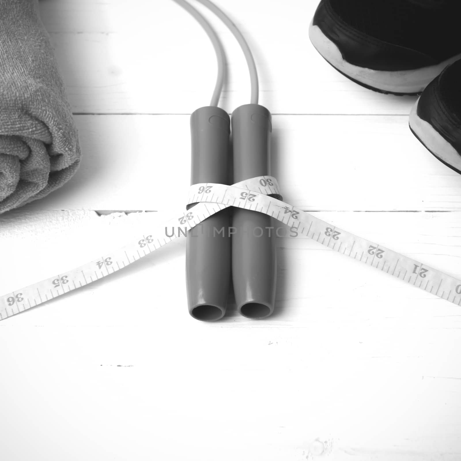 fitness equipment : running shoes,towel,jumping rope and measuring tape on white wood table black and white color tone style