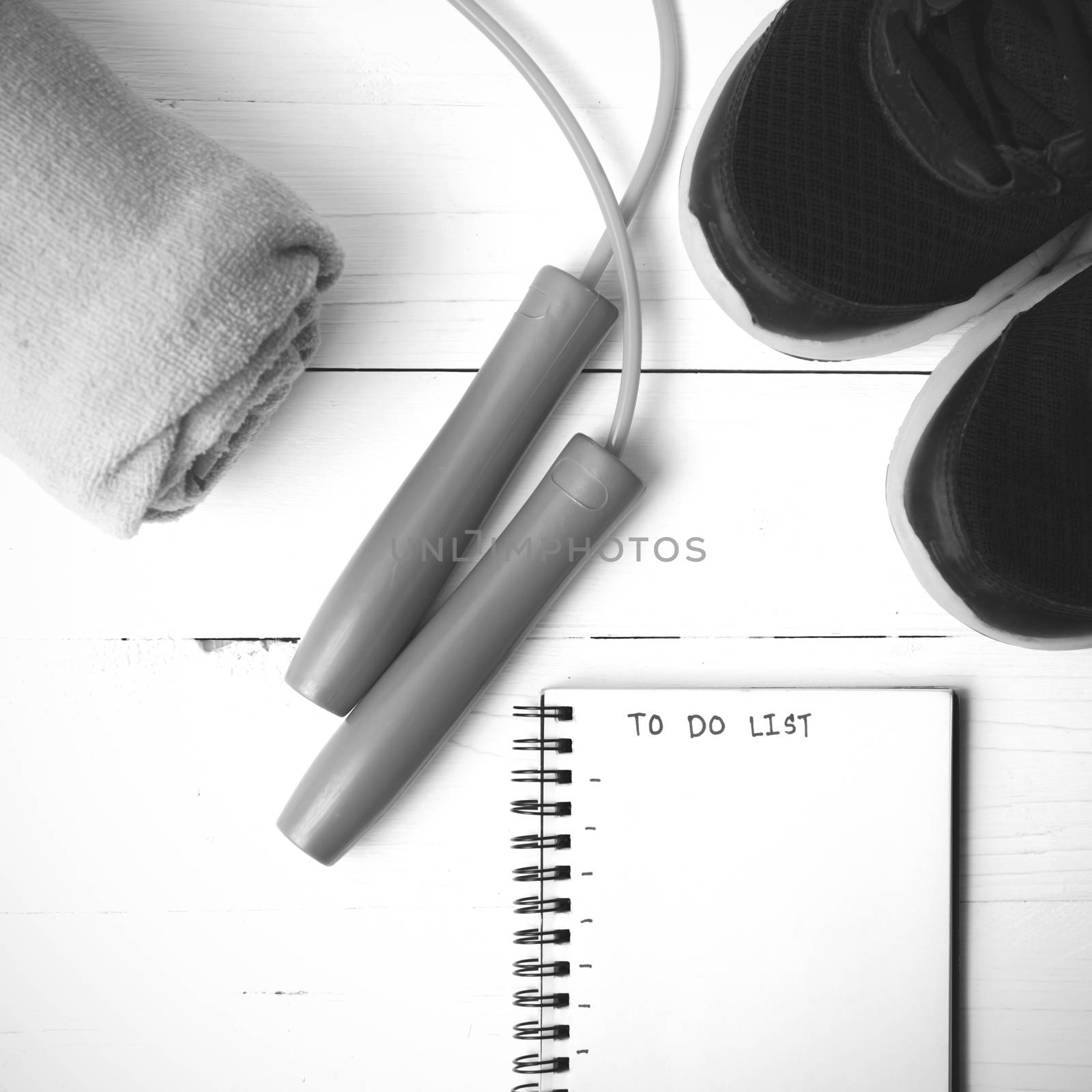 fitness equipment : running shoes,towel,jumping rope and notebook write to do list on white wood table black and white color tone style