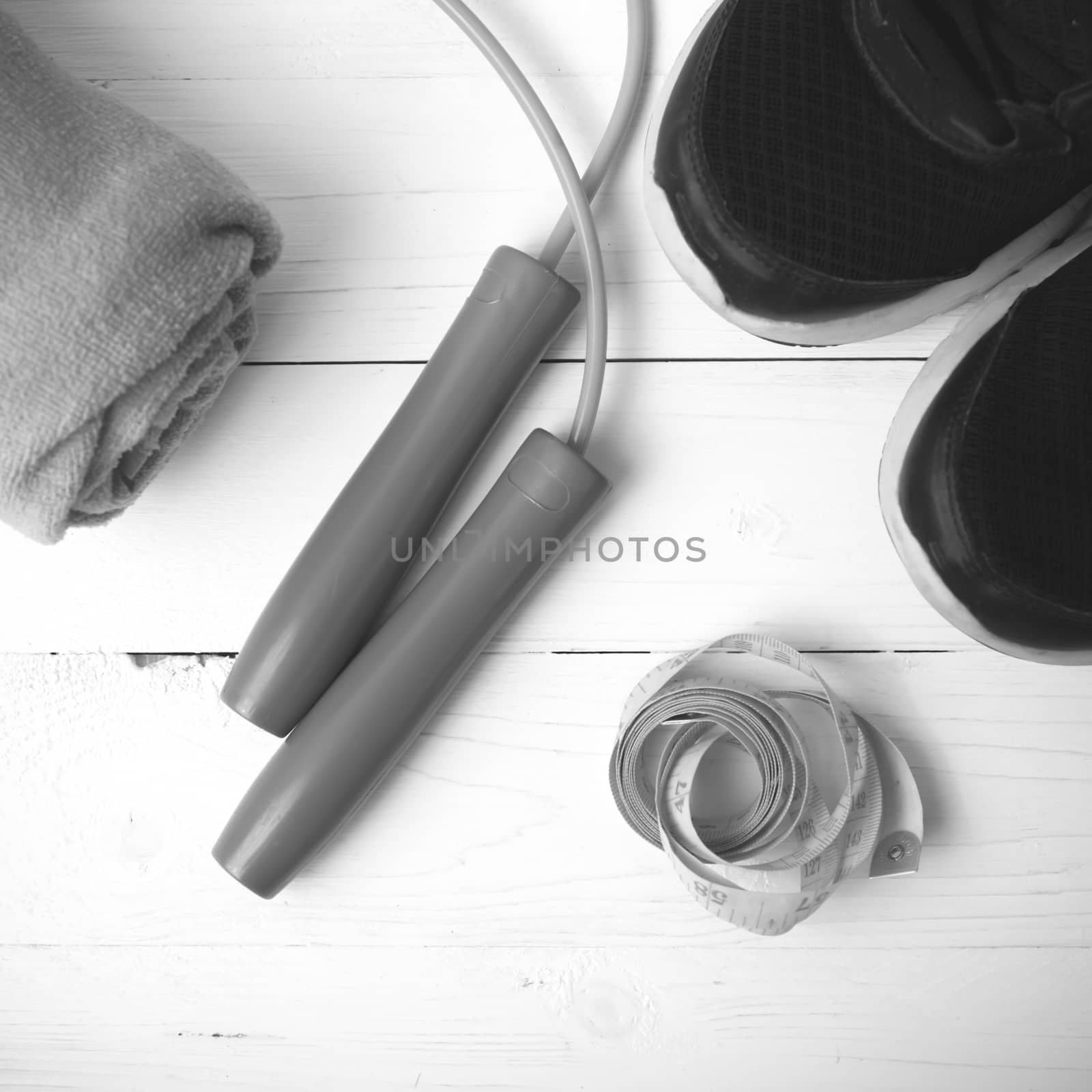 fitness equipment : running shoes,towel,jumping rope and measuring tape on white wood table black and white color tone style