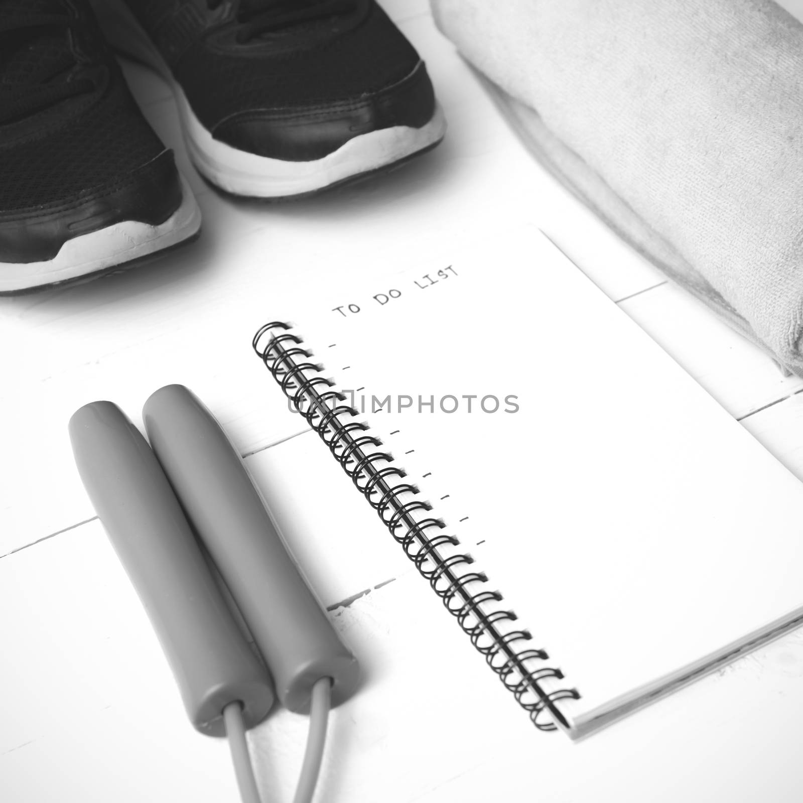 fitness equipment : running shoes,towel,jumping rope and notebook write to do list on white wood table black and white color tone style