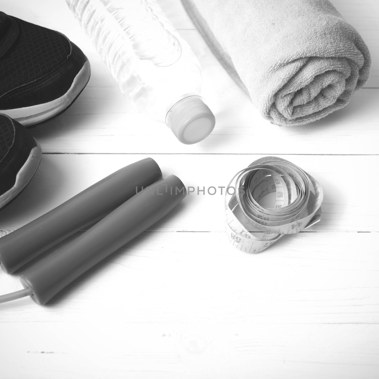 fitness equipment : running shoes,towel,jumping rope,water bottle and measuring tape on white wood table black and white color tone style