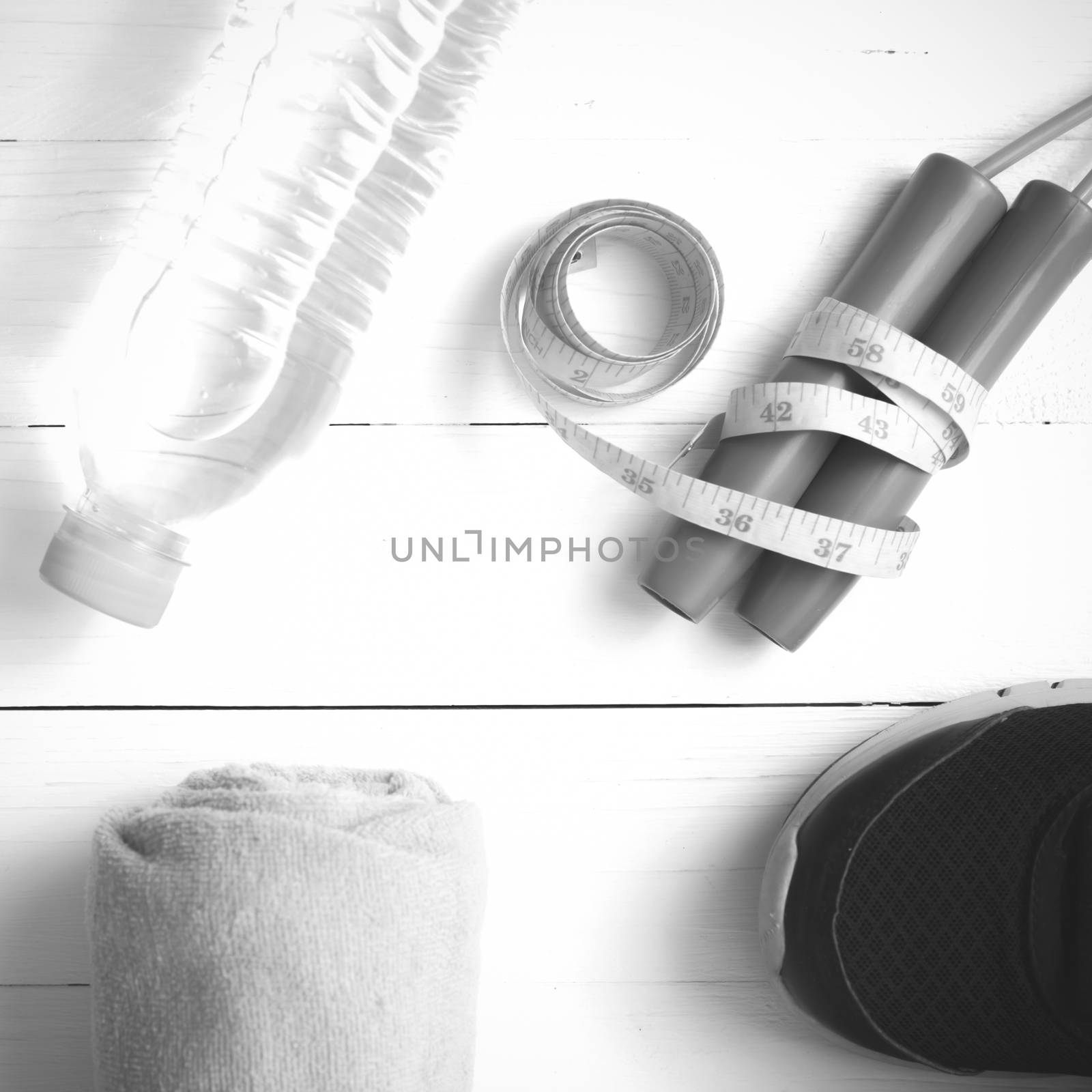 fitness equipment : running shoes,towel,jumping rope,water bottle and measuring tape on white wood table black and white color tone style