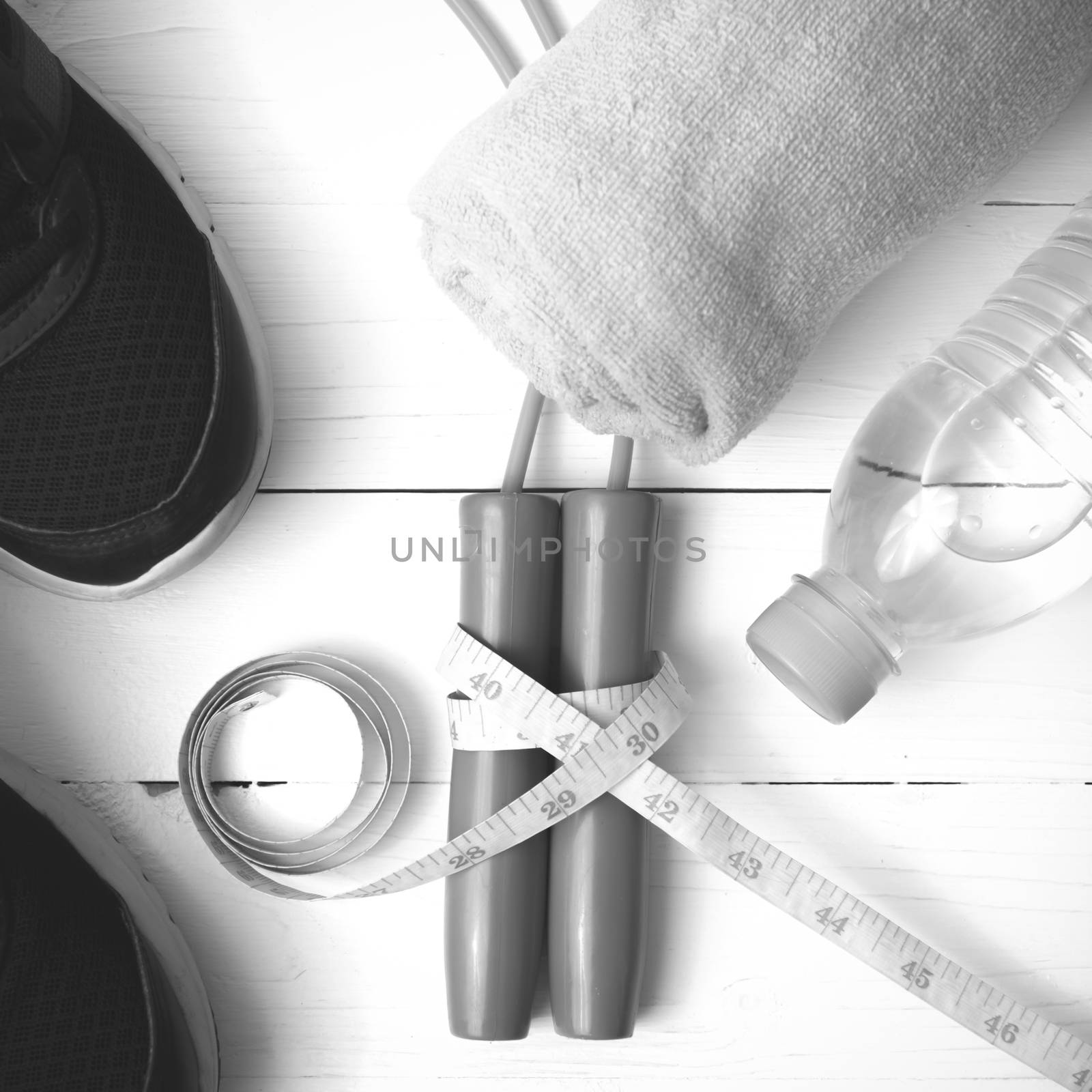 fitness equipment : running shoes,towel,jumping rope,water bottle and measuring tape on white wood table black and white color tone style