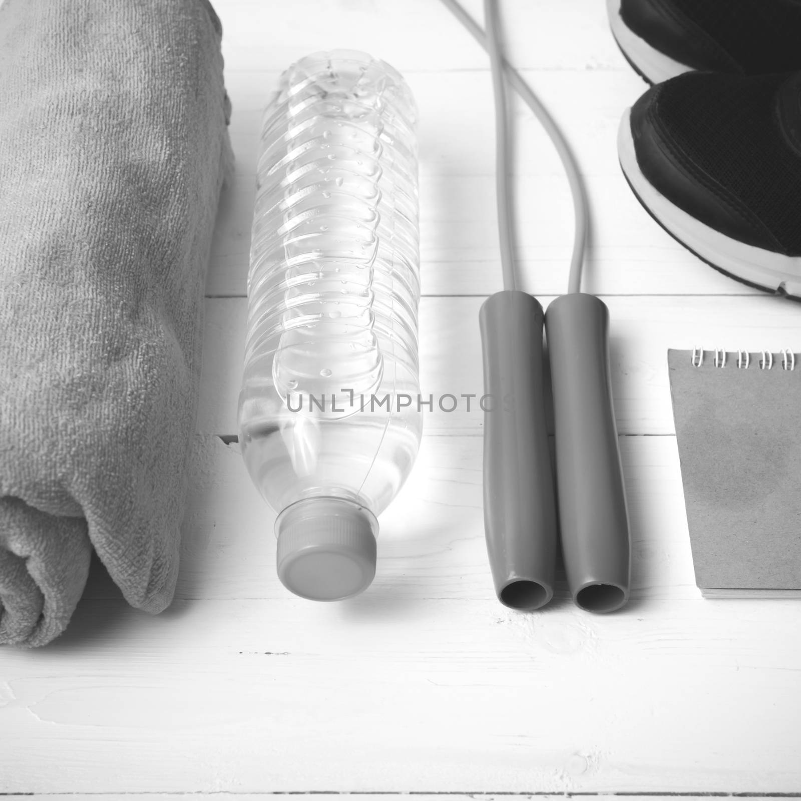 fitness equipment : running shoes,towel,jumping rope,water bottle and notepad on white wood table black and white color tone style