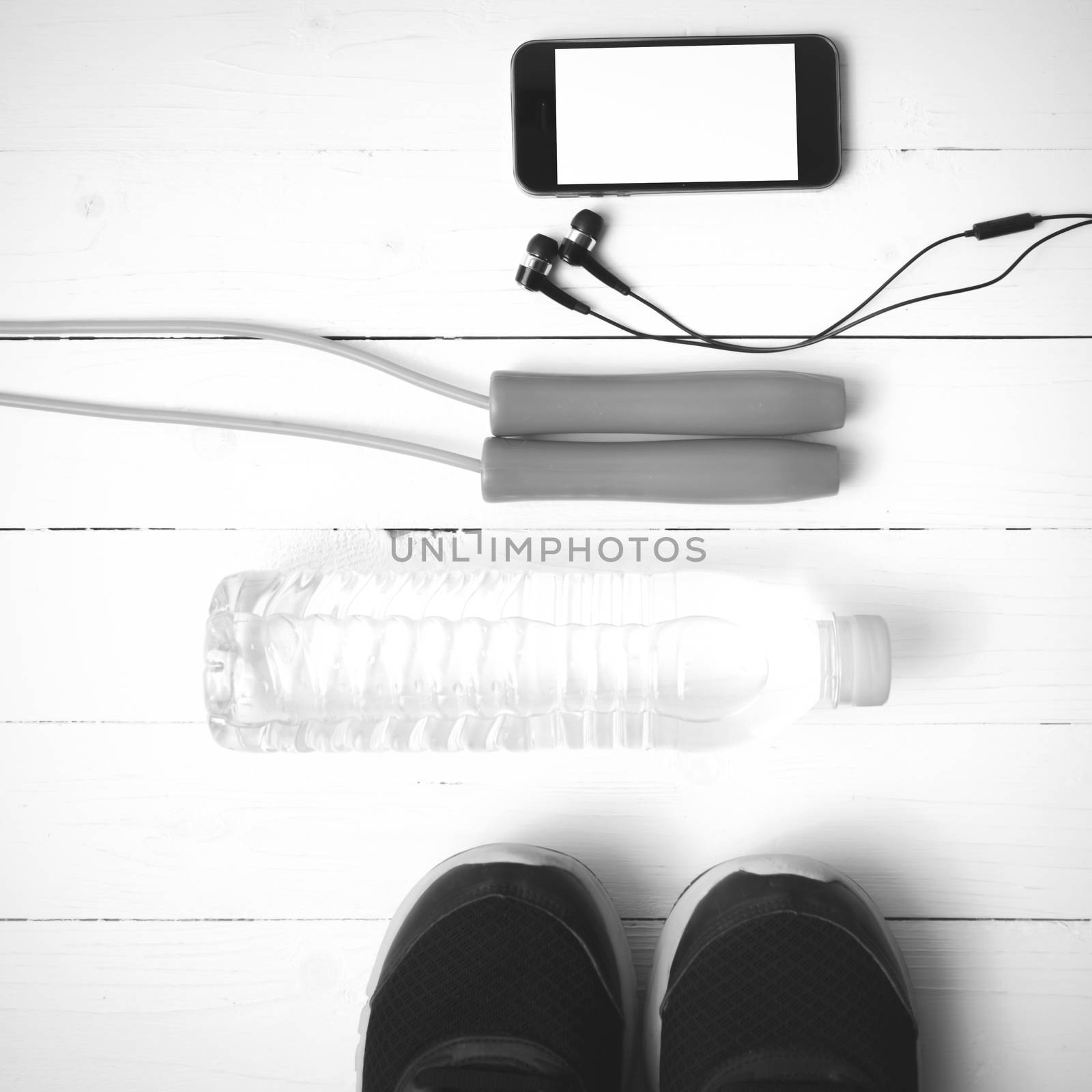 fitness equipment : running shoes,jumping rope,water bottle and phone on white wood table black and white color tone style