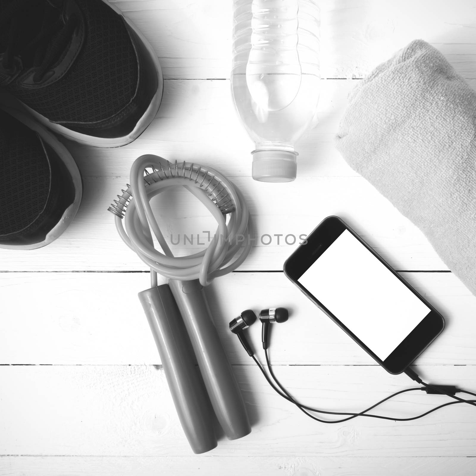fitness equipment : running shoes,towel,jumping rope,water bottle and phone on white wood table black and white color tone style