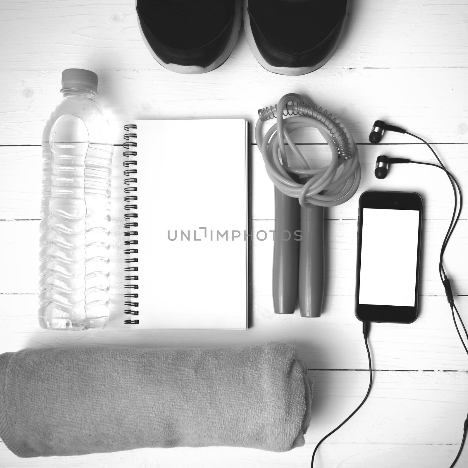 fitness equipment : running shoes,towel,jumping rope,water bottle,phone and notepad on white wood table black and white color tone style