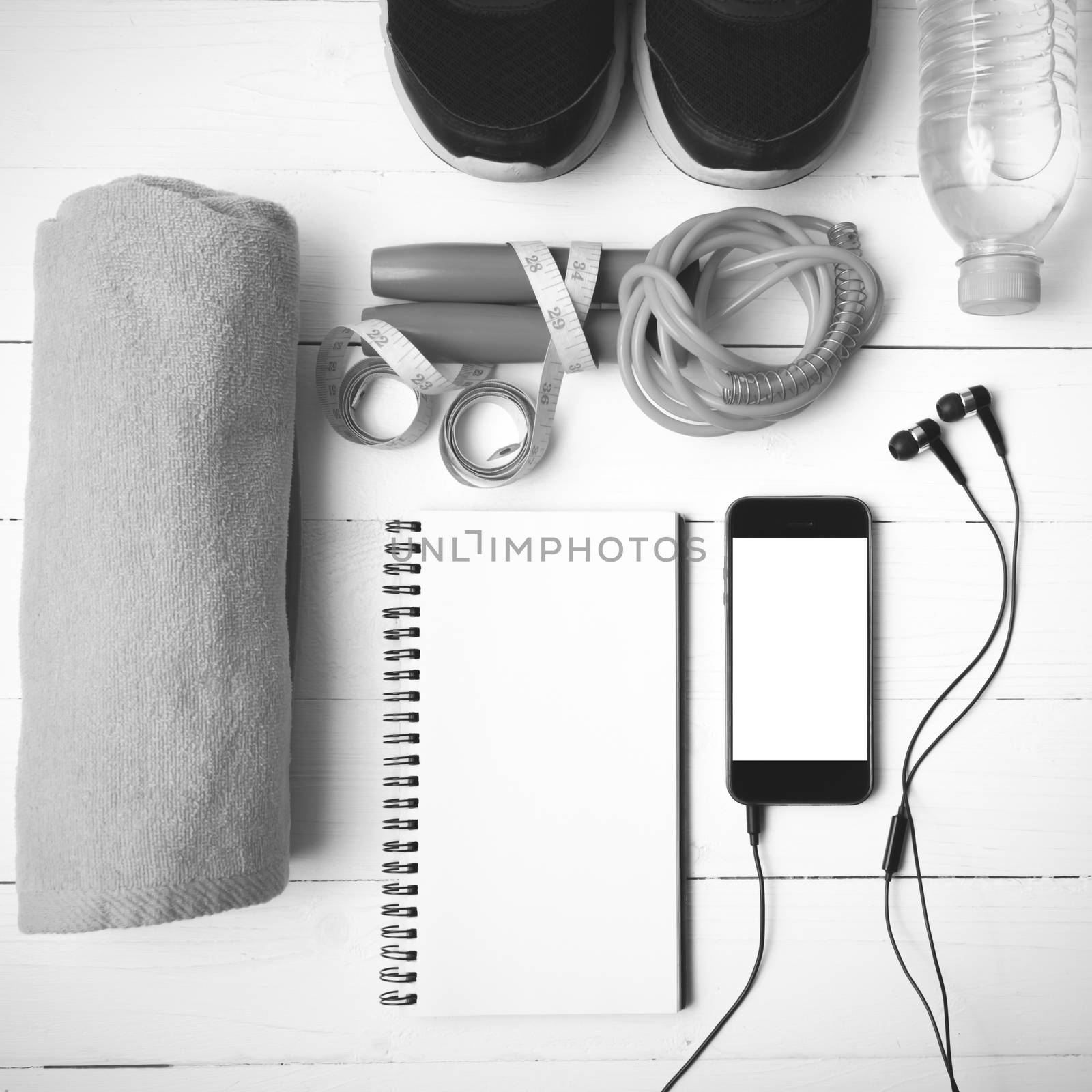 fitness equipment : running shoes,towel,jumping rope,water bottle,phone,notepad and measuring tape on white wood table black and white color tone style