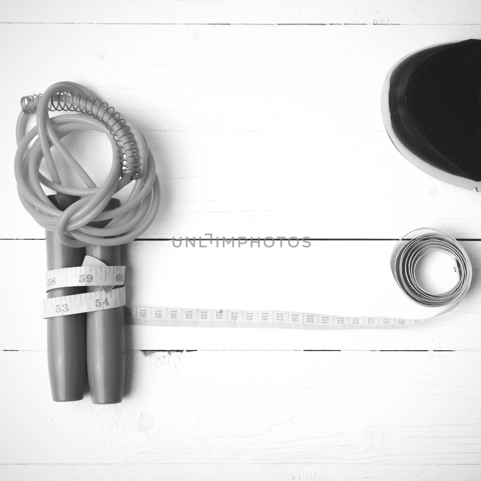 fitness equipment : running shoes,jumping rope and measuring tape on white wood table black and white color tone style