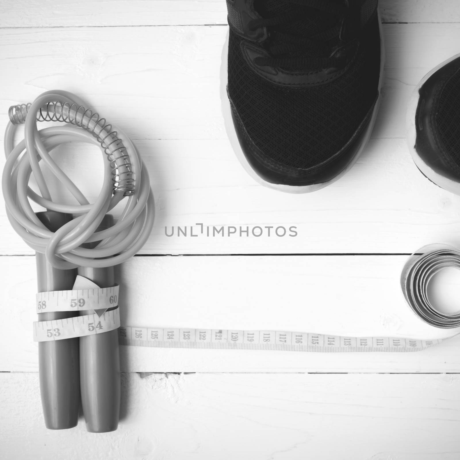 fitness equipment : running shoes,jumping rope and measuring tape on white wood table black and white color tone style