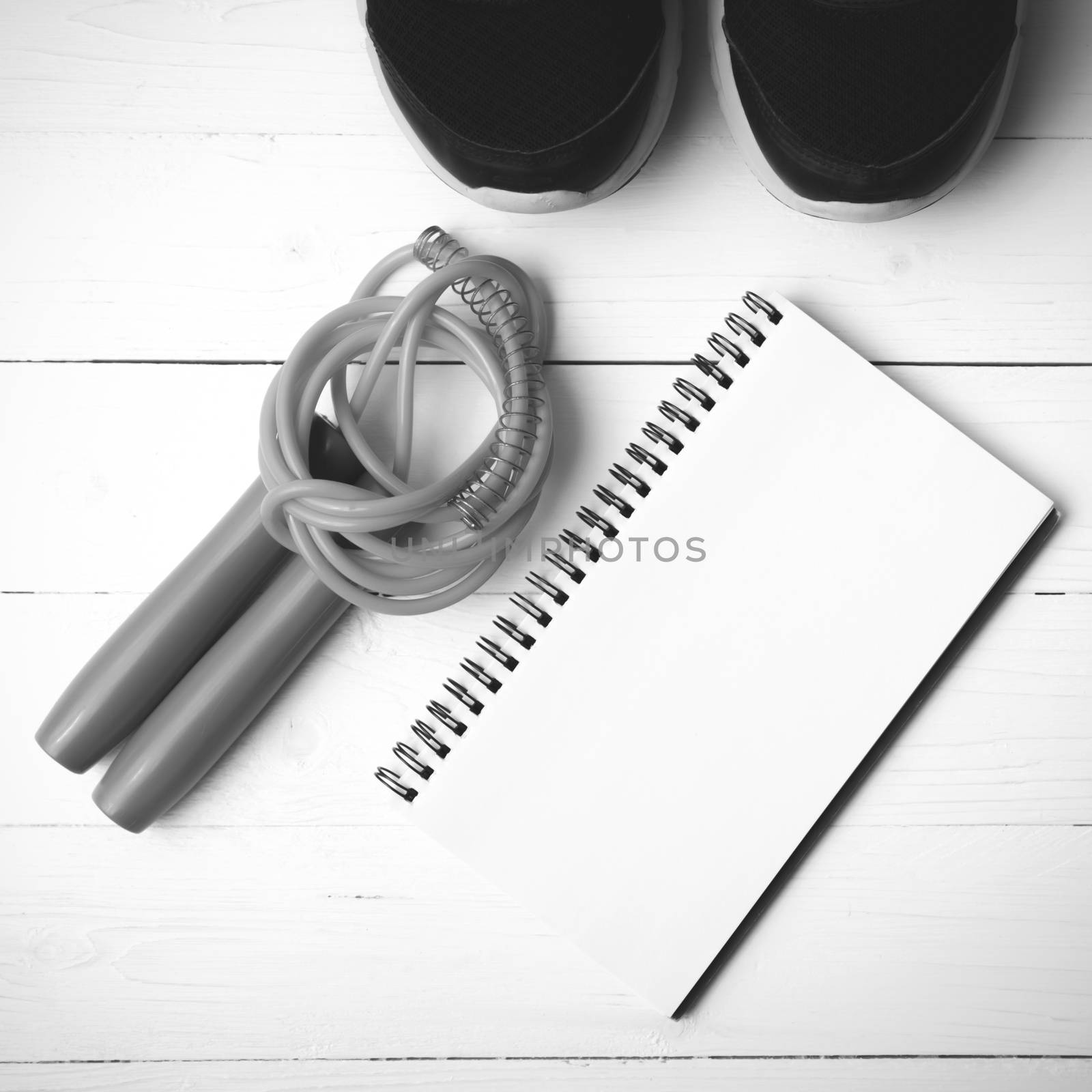 fitness equipment : running shoes,jumping rope and notepad on white wood table black and white color tone style