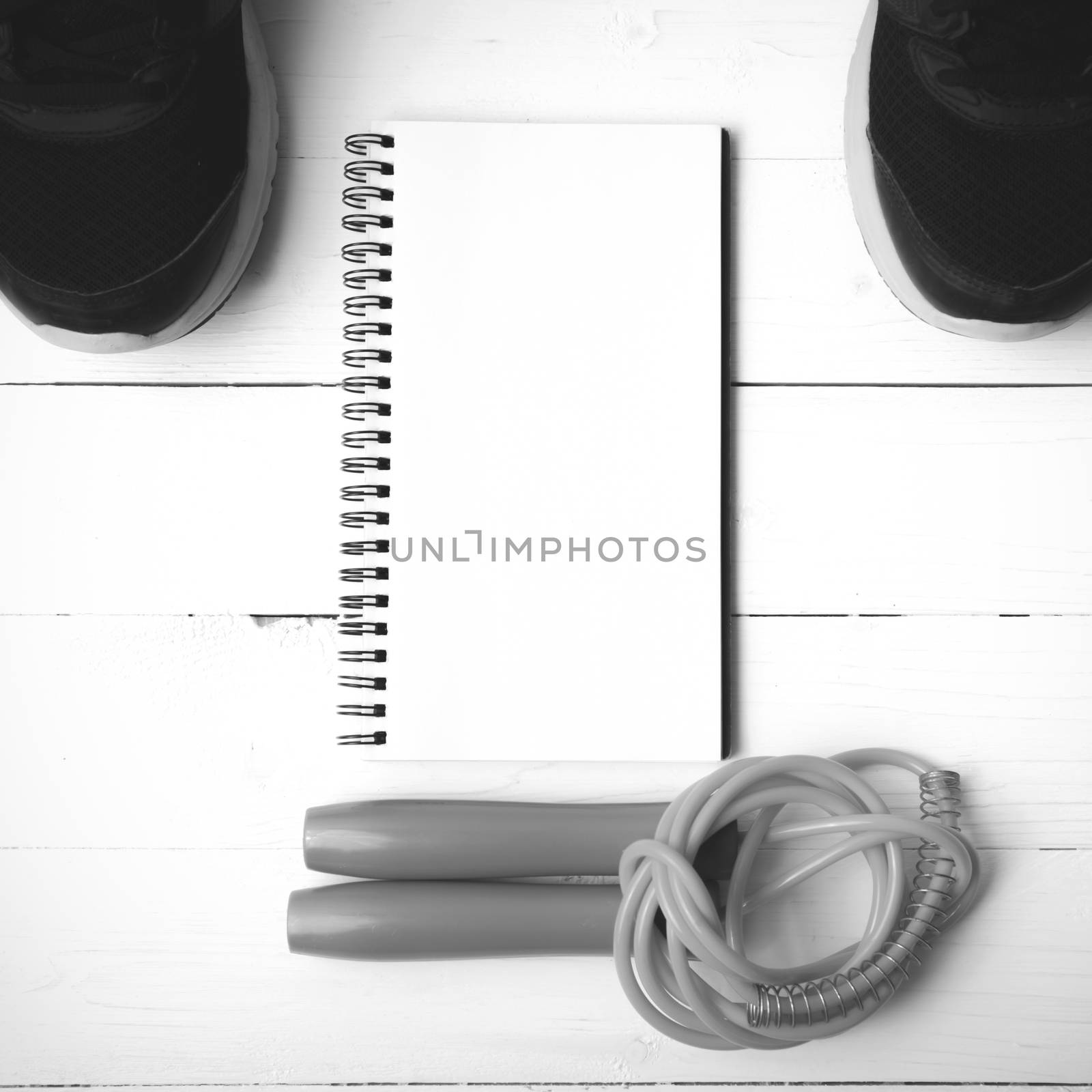 fitness equipment : running shoes,jumping rope and notepad on white wood table black and white color tone style