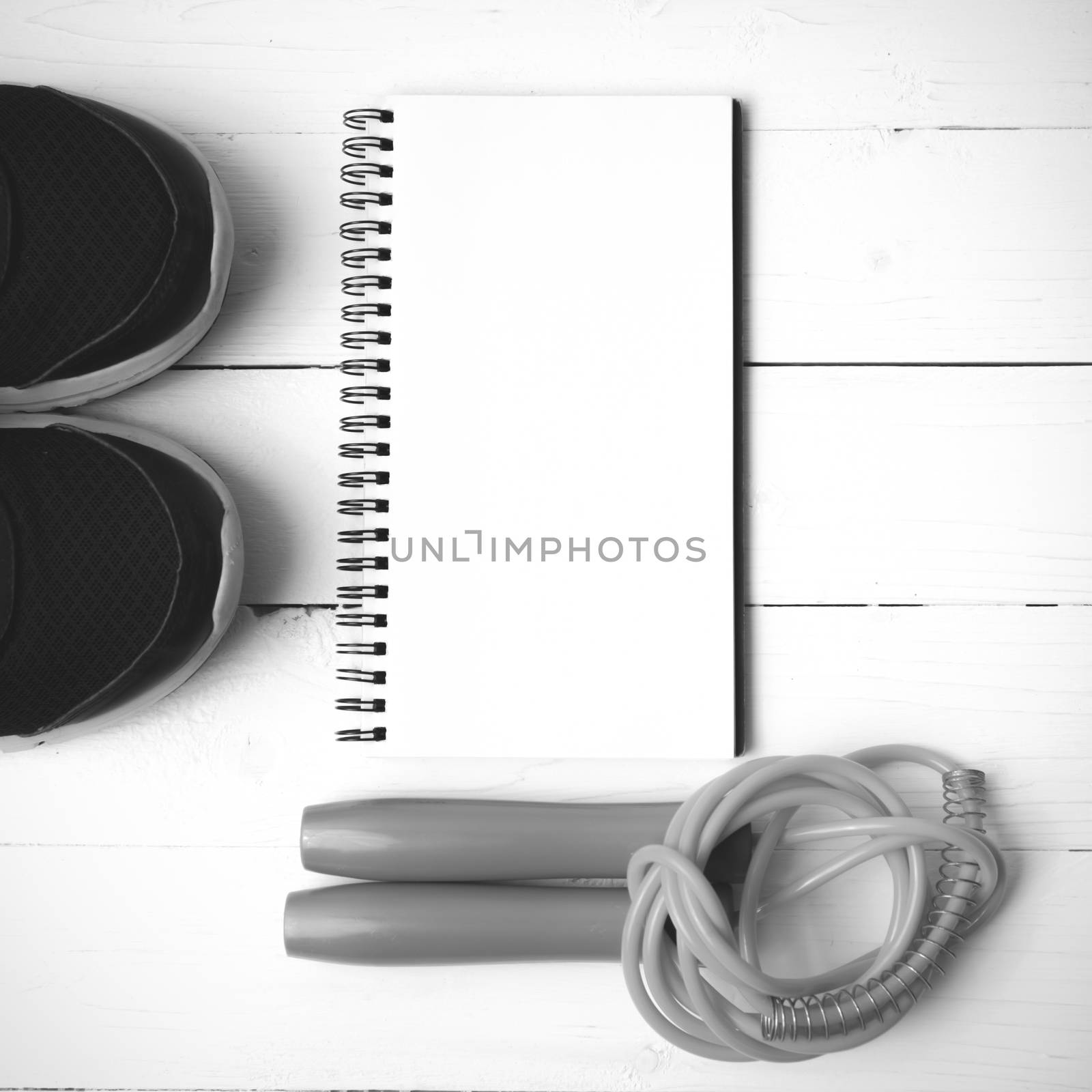 fitness equipment : running shoes,jumping rope and notepad on white wood table black and white color tone style