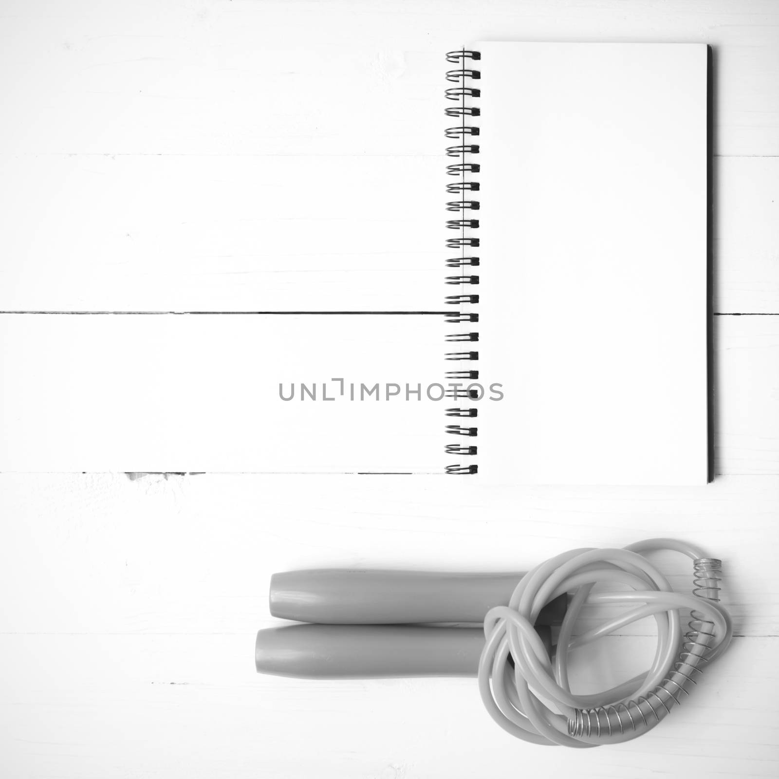 fitness equipment : jumping rope and notepad on white wood table black and white color tone style