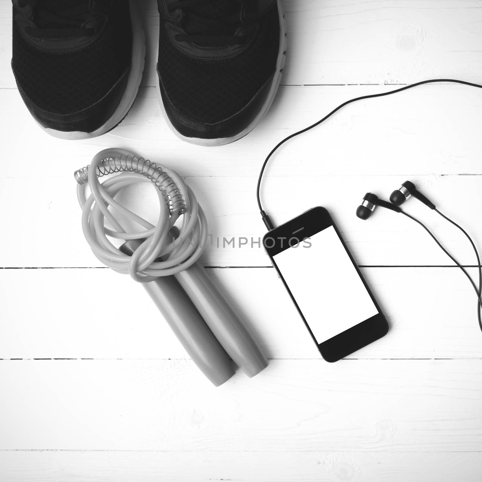 fitness equipment : running shoes,jumping rope and phone on white wood table black and white color tone style