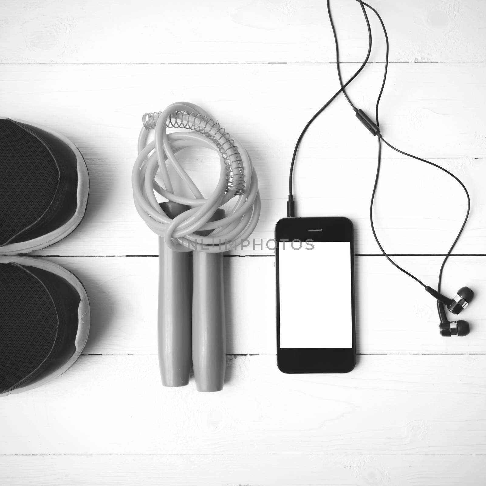 fitness equipment : running shoes,jumping rope and phone on white wood table black and white color tone style