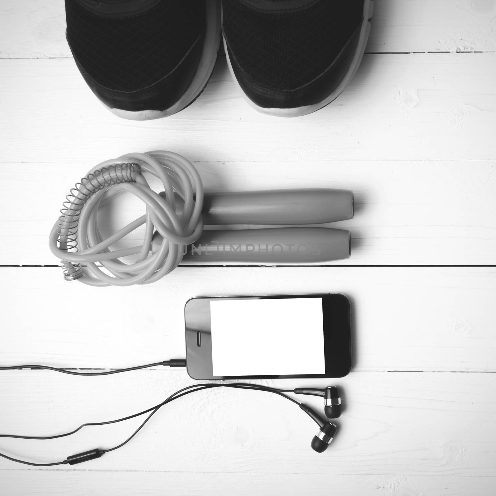 fitness equipment : running shoes,jumping rope and phone on white wood table black and white color tone style