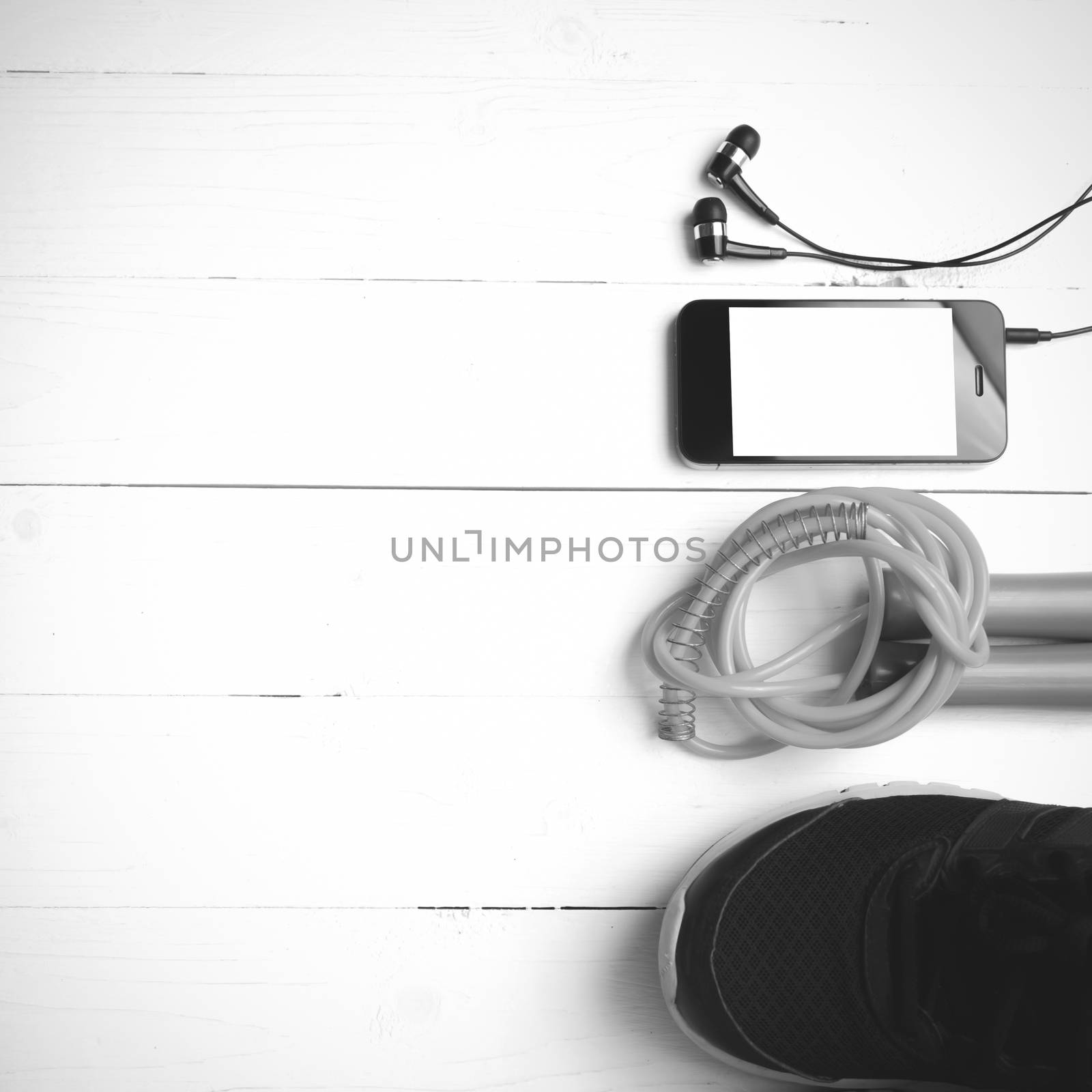 fitness equipment : running shoes,jumping rope and phone on white wood table black and white color tone style