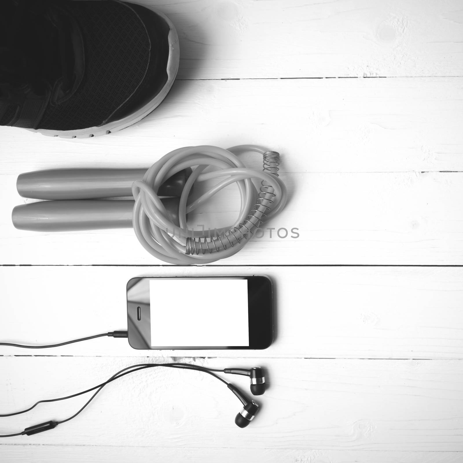 fitness equipment : running shoes,jumping rope and phone on white wood table black and white color tone style