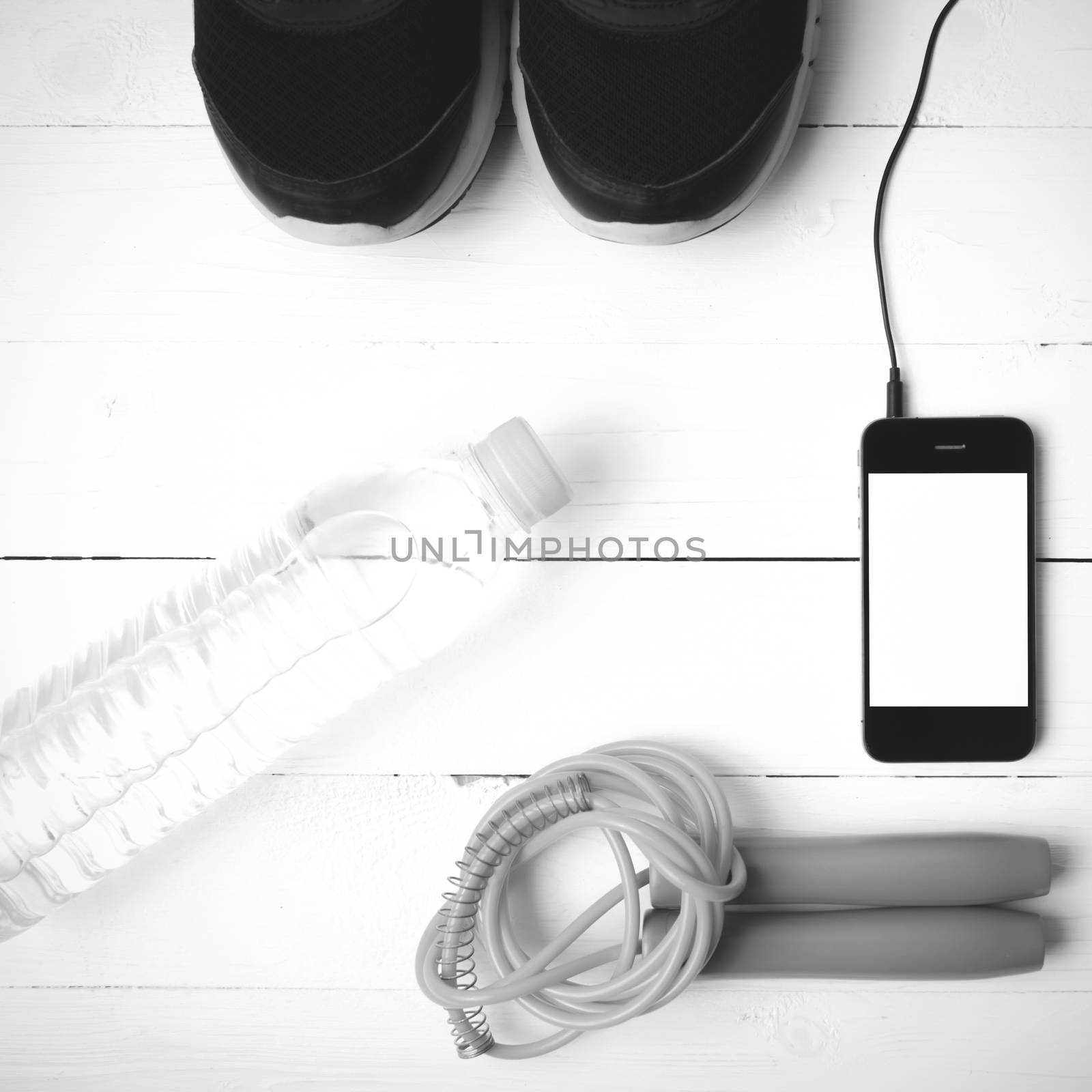 fitness equipment : running shoes,jumping rope,phone and water bottle on white wood table black and white color tone style