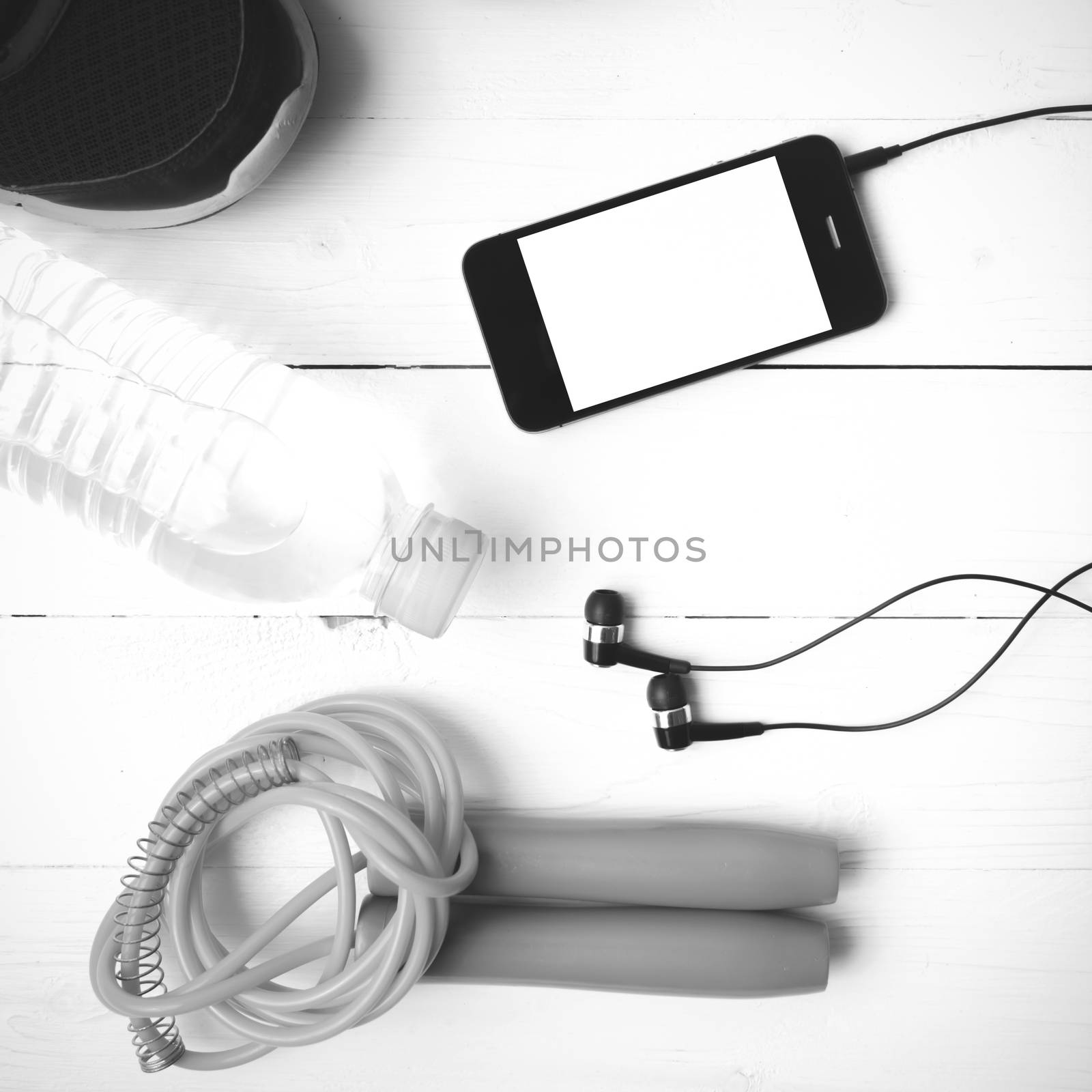 fitness equipment : running shoes,jumping rope,phone and water bottle on white wood table black and white color tone style