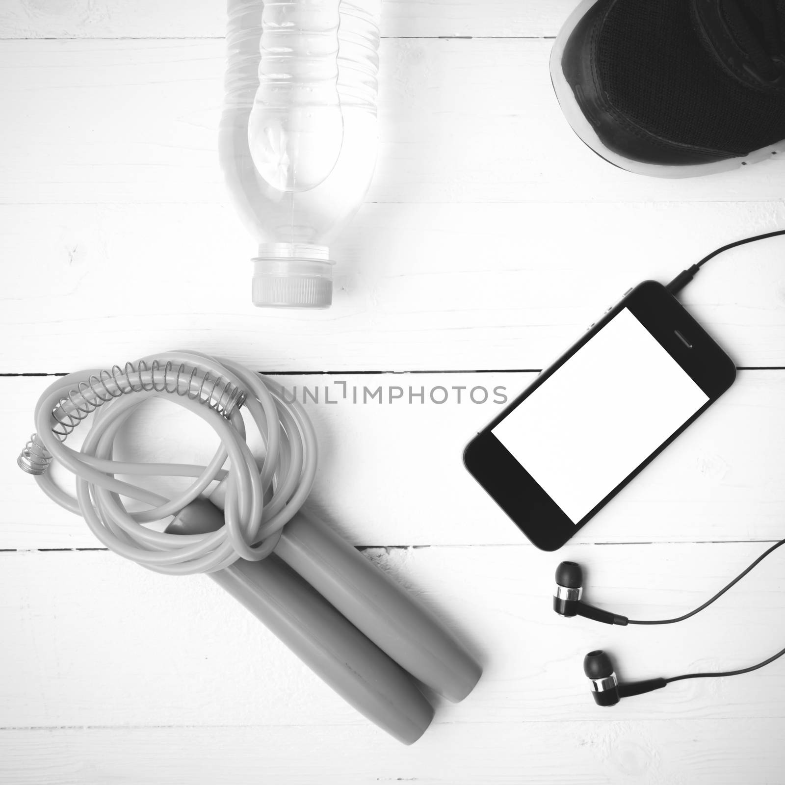 fitness equipment : running shoes,jumping rope,phone and water bottle on white wood table black and white color tone style