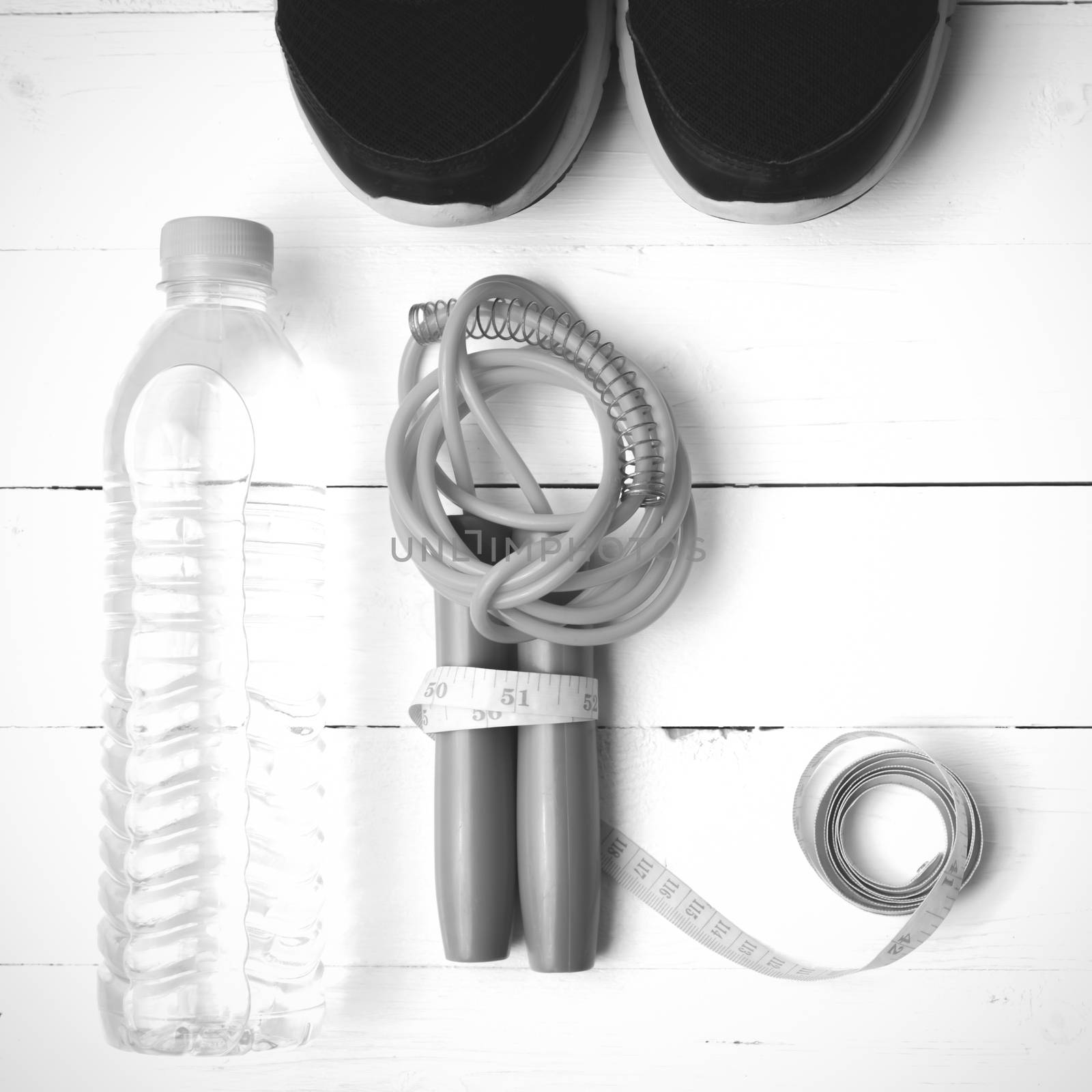 fitness equipment : running shoes,jumping rope,measuring tape and water bottle on white wood table black and white color tone style