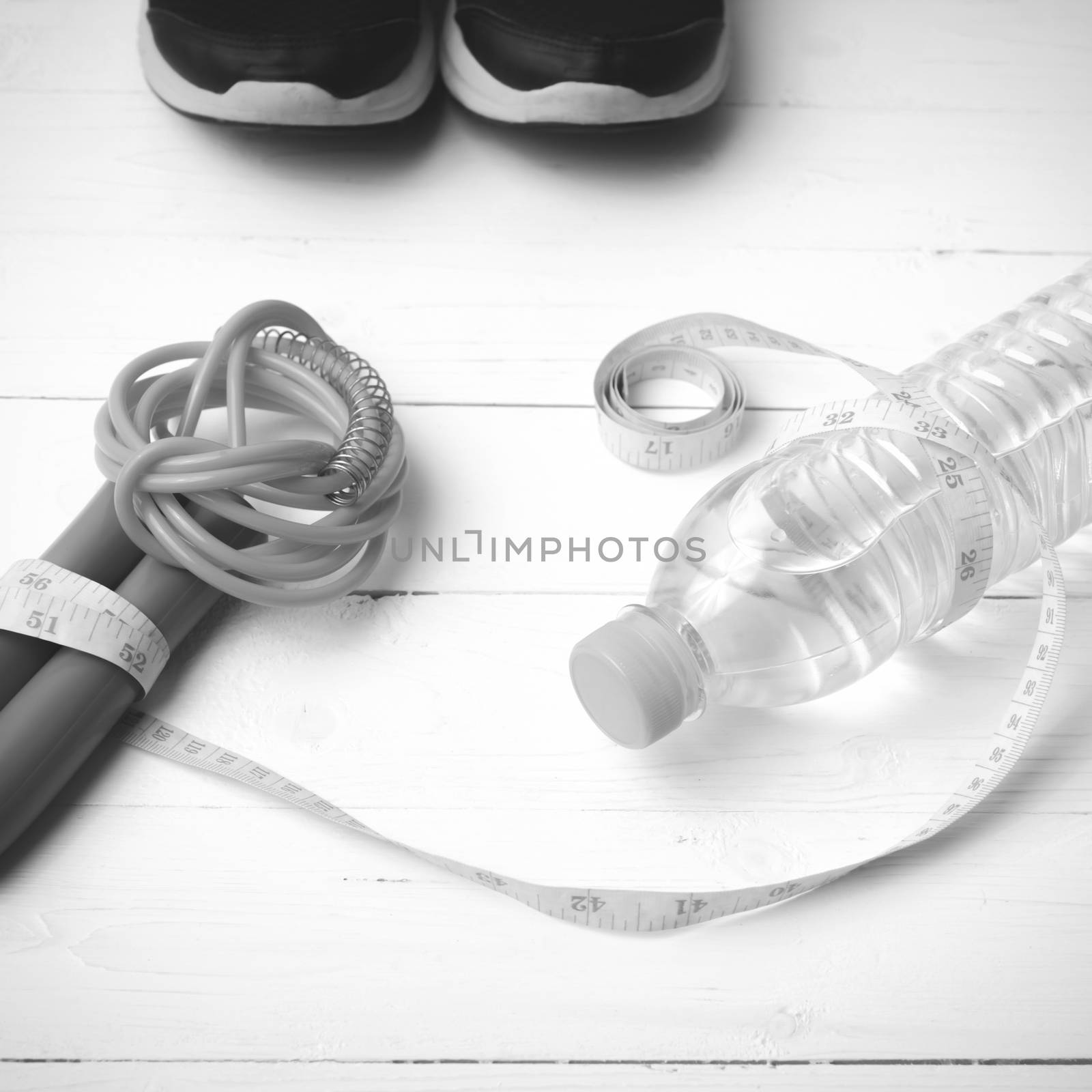 fitness equipment : running shoes,jumping rope,measuring tape and water bottle on white wood table black and white color tone style