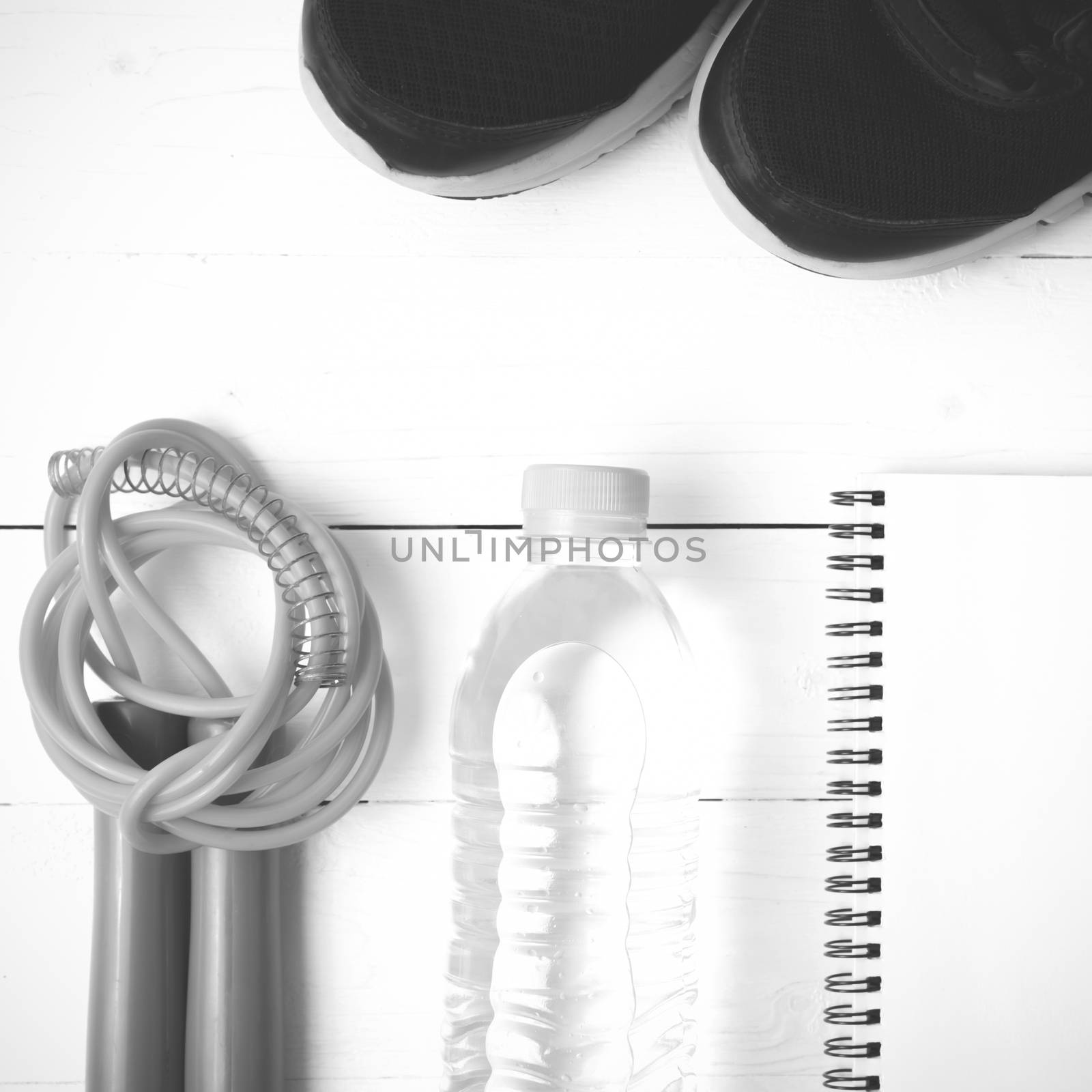 fitness equipment : running shoes,jumping rope,drinking water and notepad on white wood table  black and white tone color style