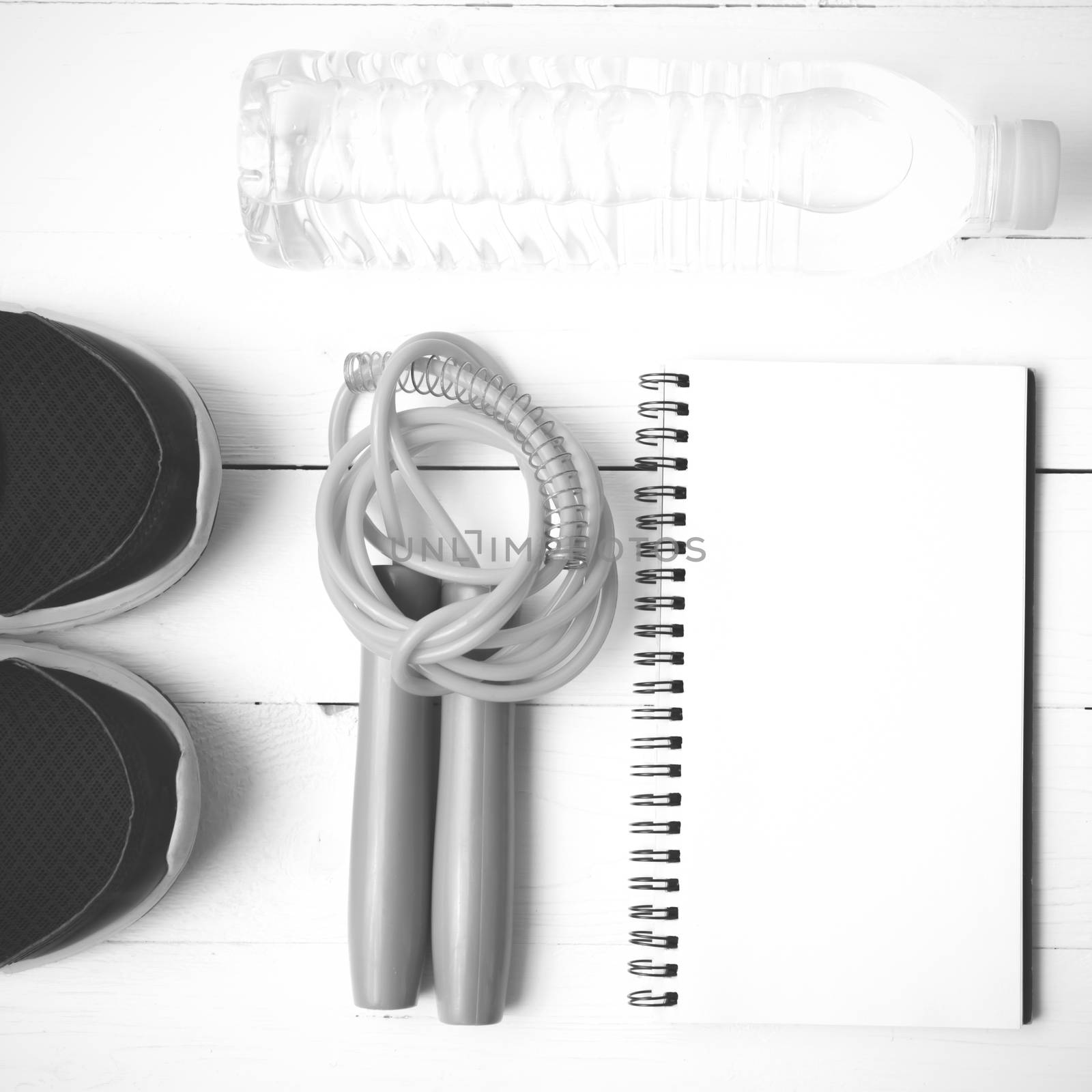 fitness equipment : running shoes,jumping rope,drinking water and notepad on white wood table  black and white tone color style