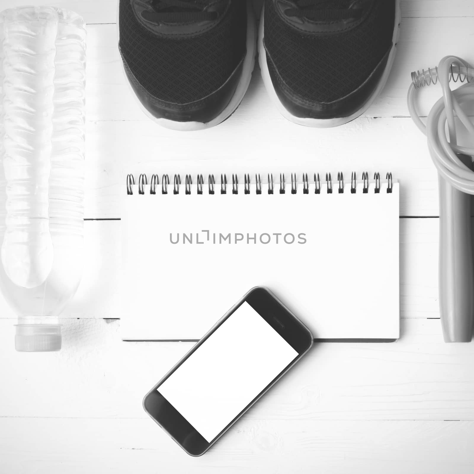 fitness equipment : running shoes,jumping rope,drinking water,notebook and phone on white wood table  black and white tone color style