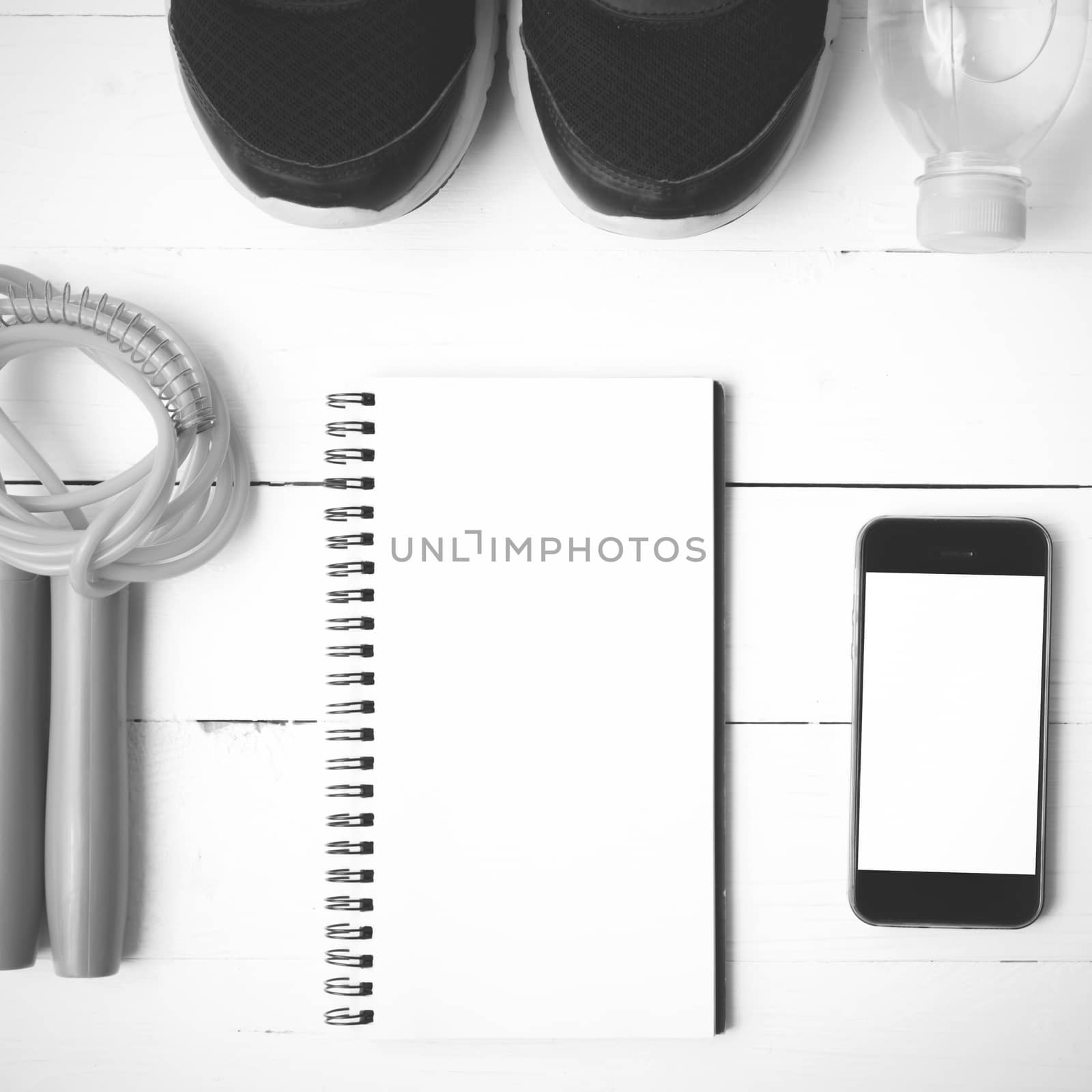 fitness equipment : running shoes,jumping rope,drinking water,notebook and phone on white wood table  black and white tone color style