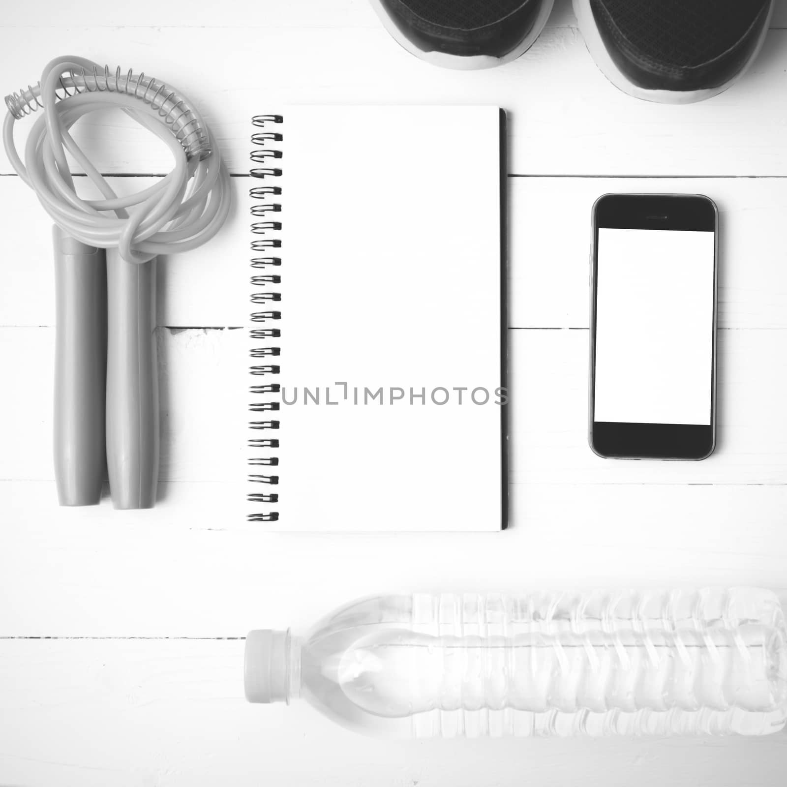 fitness equipment : running shoes,jumping rope,drinking water,notebook and phone on white wood table  black and white tone color style