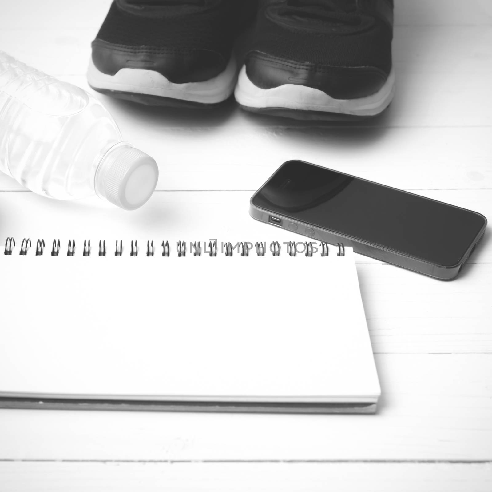 fitness equipment : running shoes,drinking water,notebook and phone on white wood table  black and white tone color style