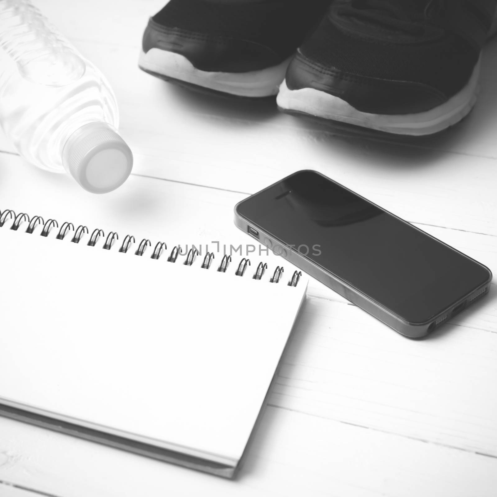 fitness equipment : running shoes,drinking water,notebook and phone on white wood table  black and white tone color style