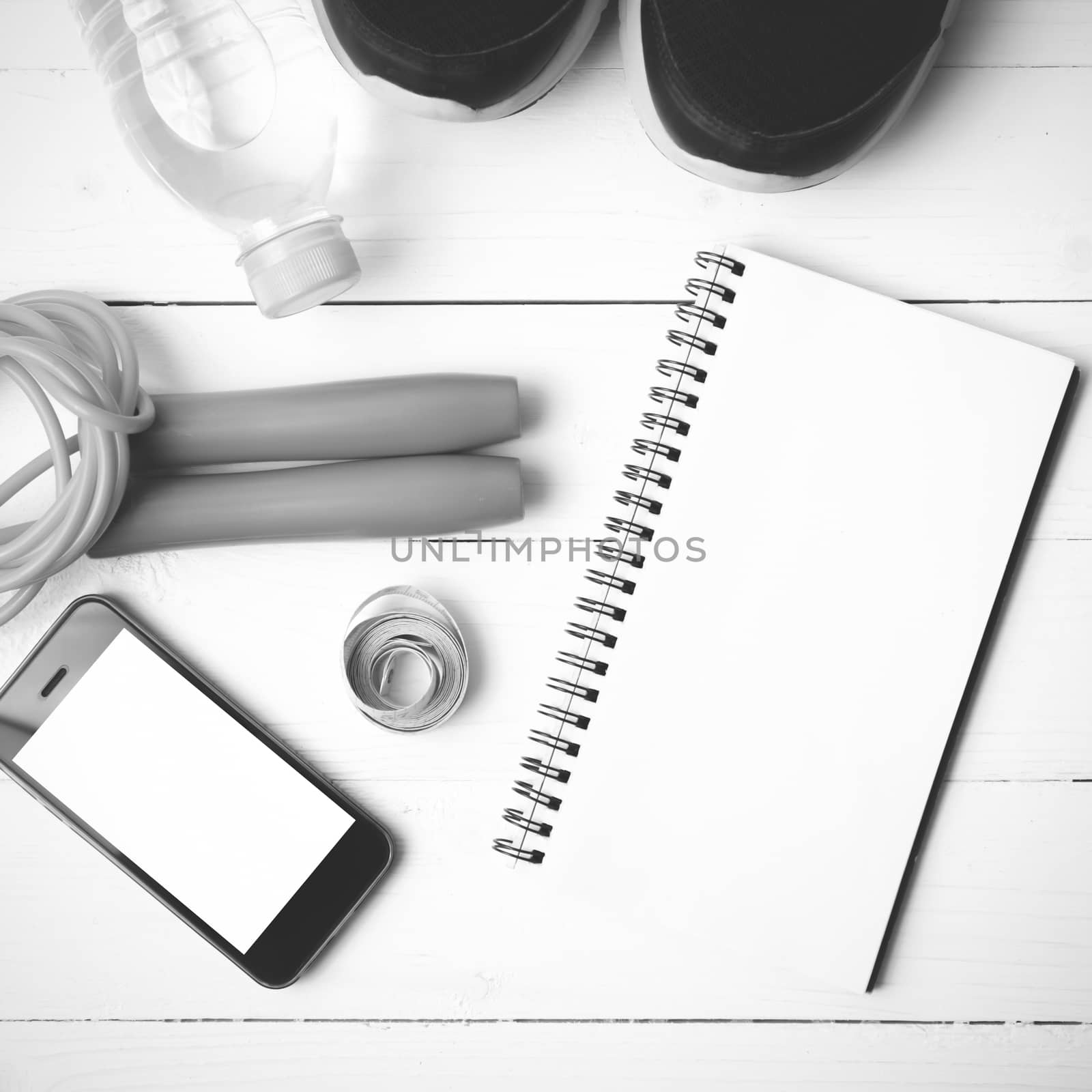 fitness equipment : running shoes,jumping rope,drinking water,notebook,measuring tape and phone on white wood table black and white tone color style