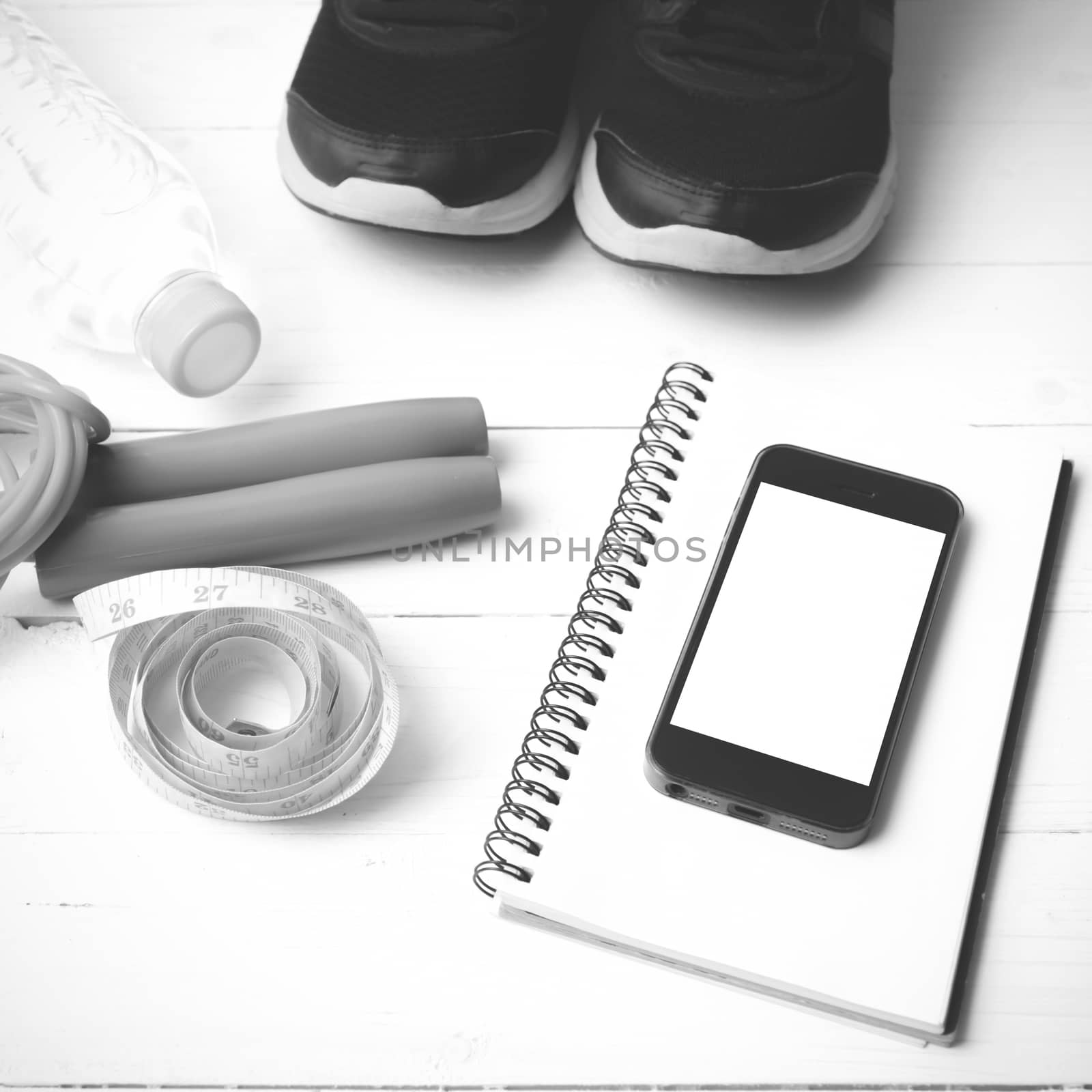 fitness equipment : running shoes,jumping rope,drinking water,notebook,measuring tape and phone on white wood table black and white tone color style