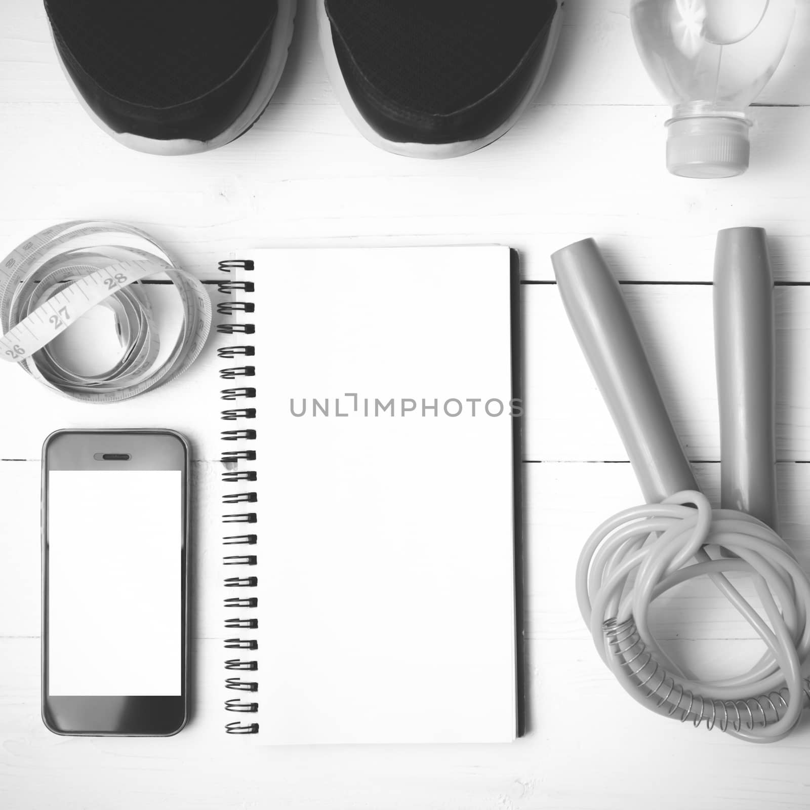 fitness equipment : running shoes,jumping rope,drinking water,notebook,measuring tape and phone on white wood table black and white tone color style