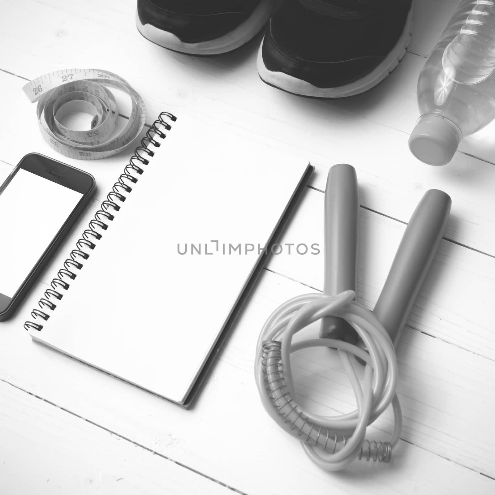 fitness equipment : running shoes,jumping rope,drinking water,notebook,measuring tape and phone on white wood table black and white tone color style