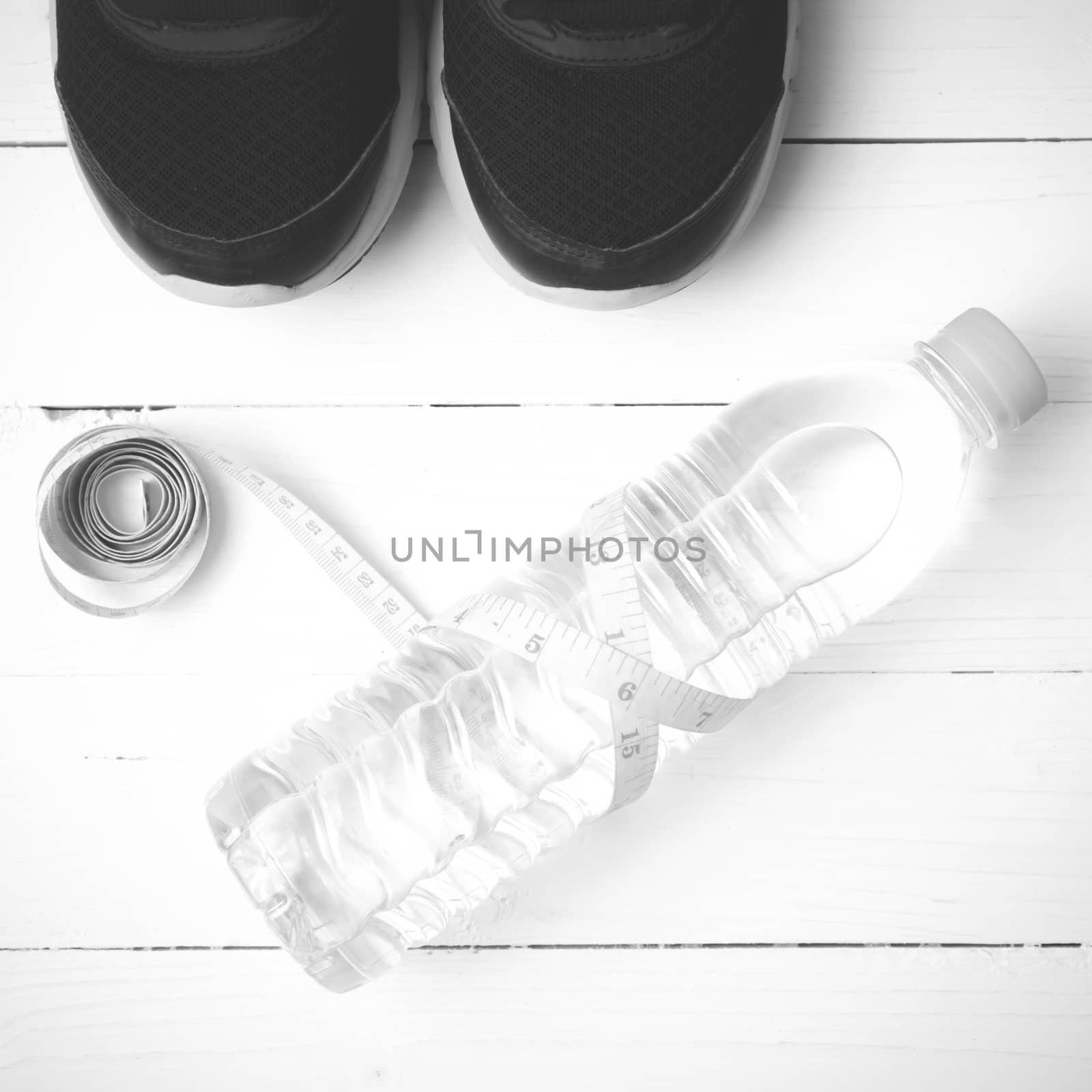 fitness equipment : running shoes,drinking water and measuring tape on white wood table black and white tone color style