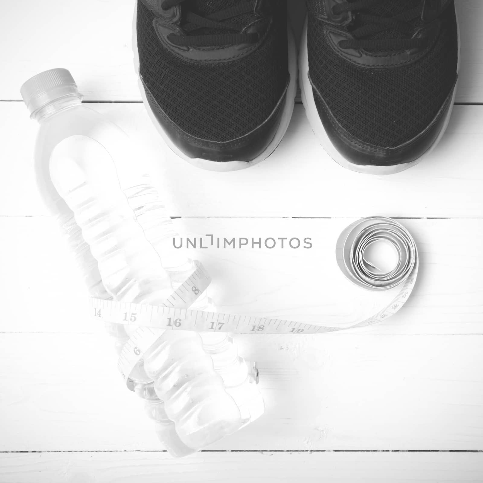 fitness equipment : running shoes,drinking water and measuring tape on white wood table black and white tone color style