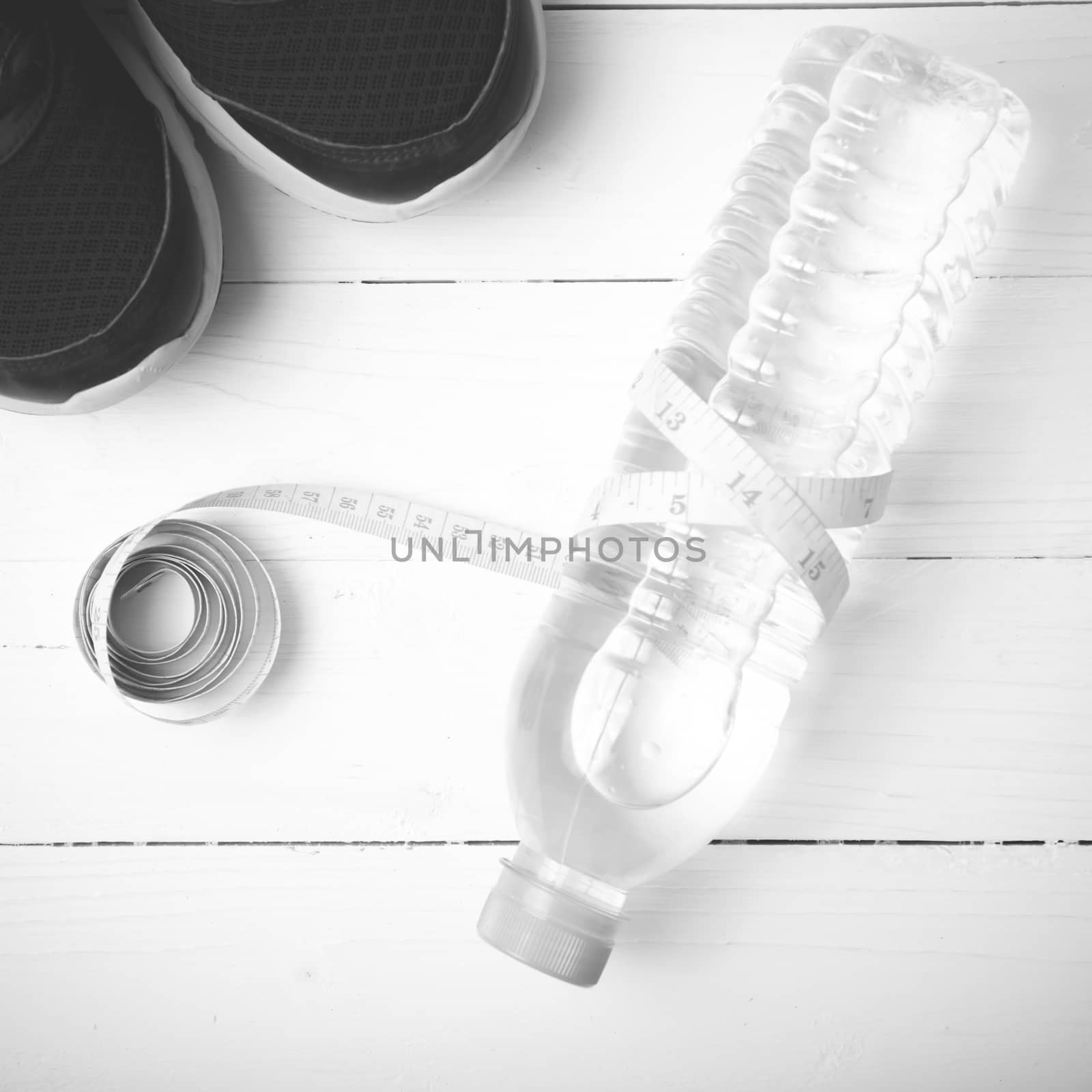 fitness equipment : running shoes,drinking water and measuring tape on white wood table black and white tone color style