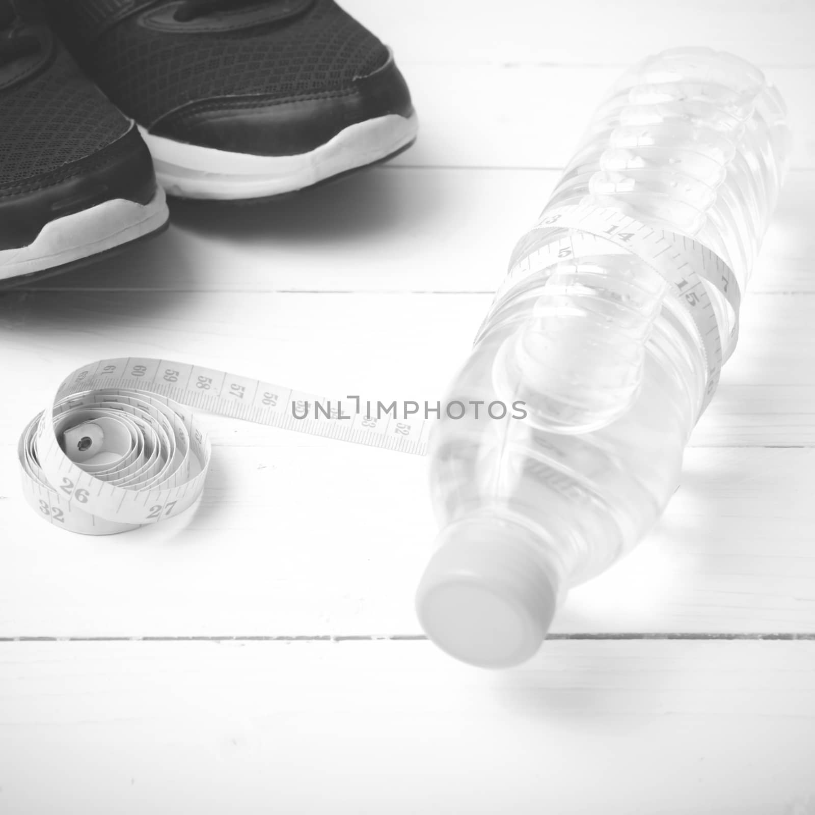 fitness equipment : running shoes,drinking water and measuring tape on white wood table black and white tone color style