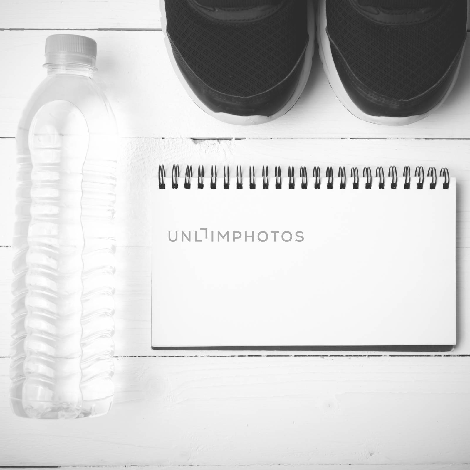 fitness equipment : running shoes,drinking water and notebook on white wood table black and white tone color style