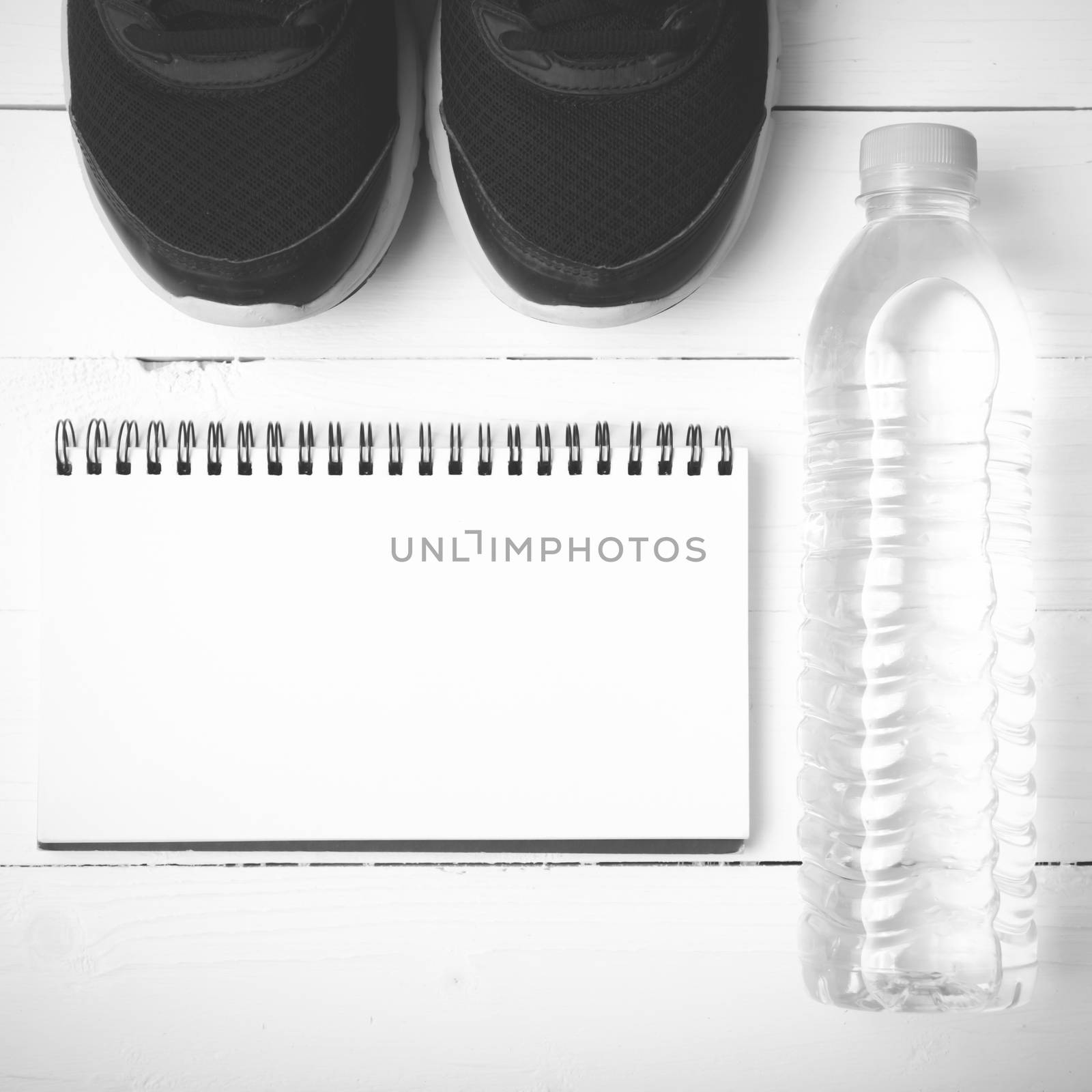 fitness equipment : running shoes,drinking water and notebook on white wood table black and white tone color style