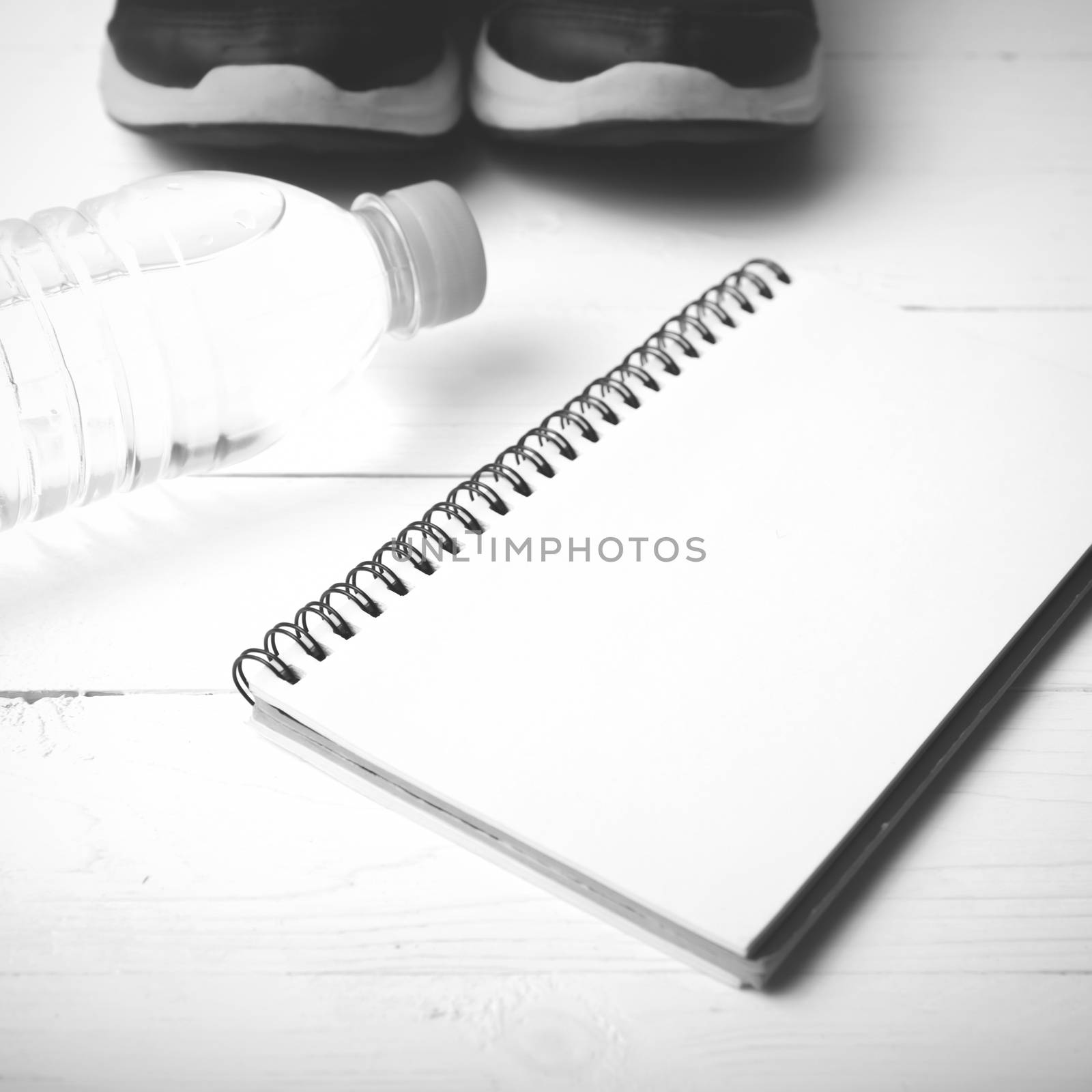 fitness equipment : running shoes,drinking water and notebook on white wood table black and white tone color style