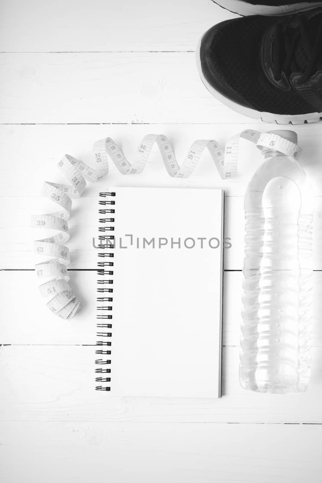 running shoes,measuring tape,drinking water and notebook on white wood table black and white tone color style